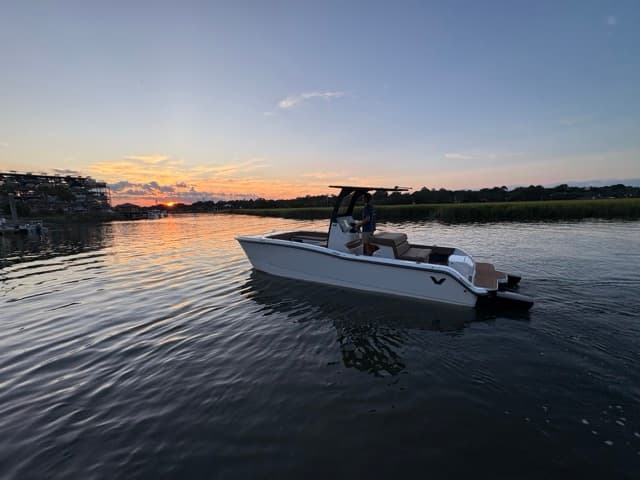 Volare Artemis 23 cruising on calm water at sunset, shown in side view from the shore.