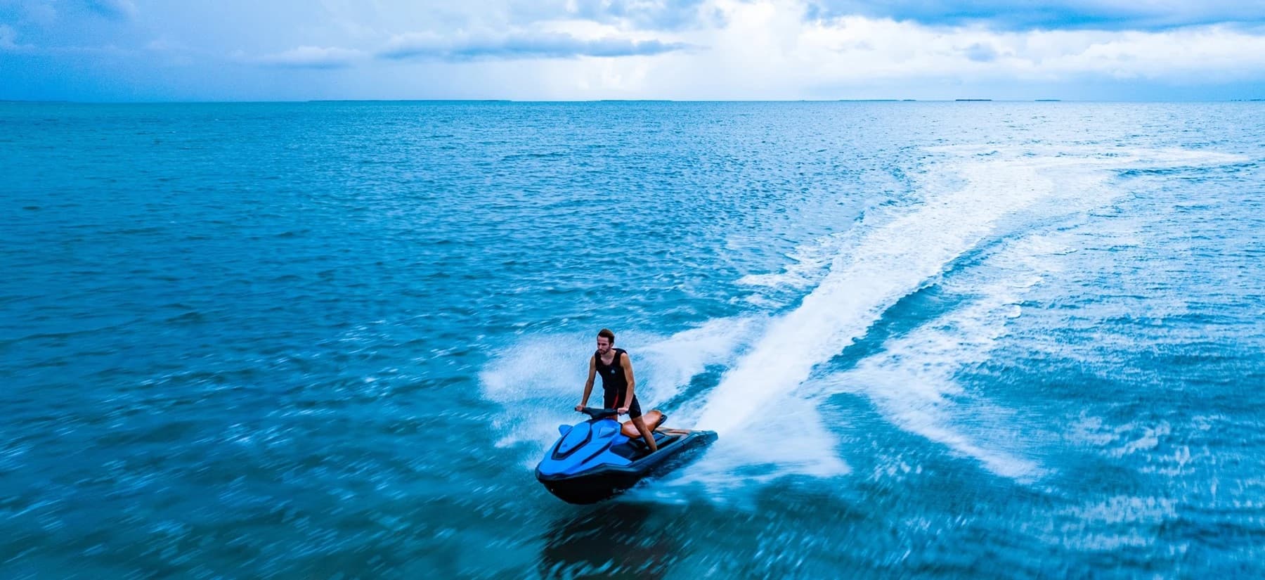 Personal watercraft (2026 Taiga Orca WX3) speeding across open water, viewed from above and behind, leaving a broad white wake.