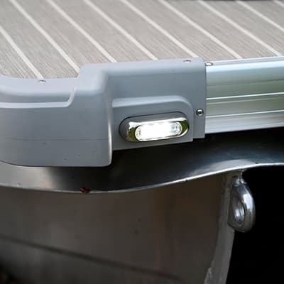 Close-up of a pontoon boat’s (2026 Princecraft Vectra 19 L) illuminated side light and aluminum railing at the stern corner, viewed from the side.
