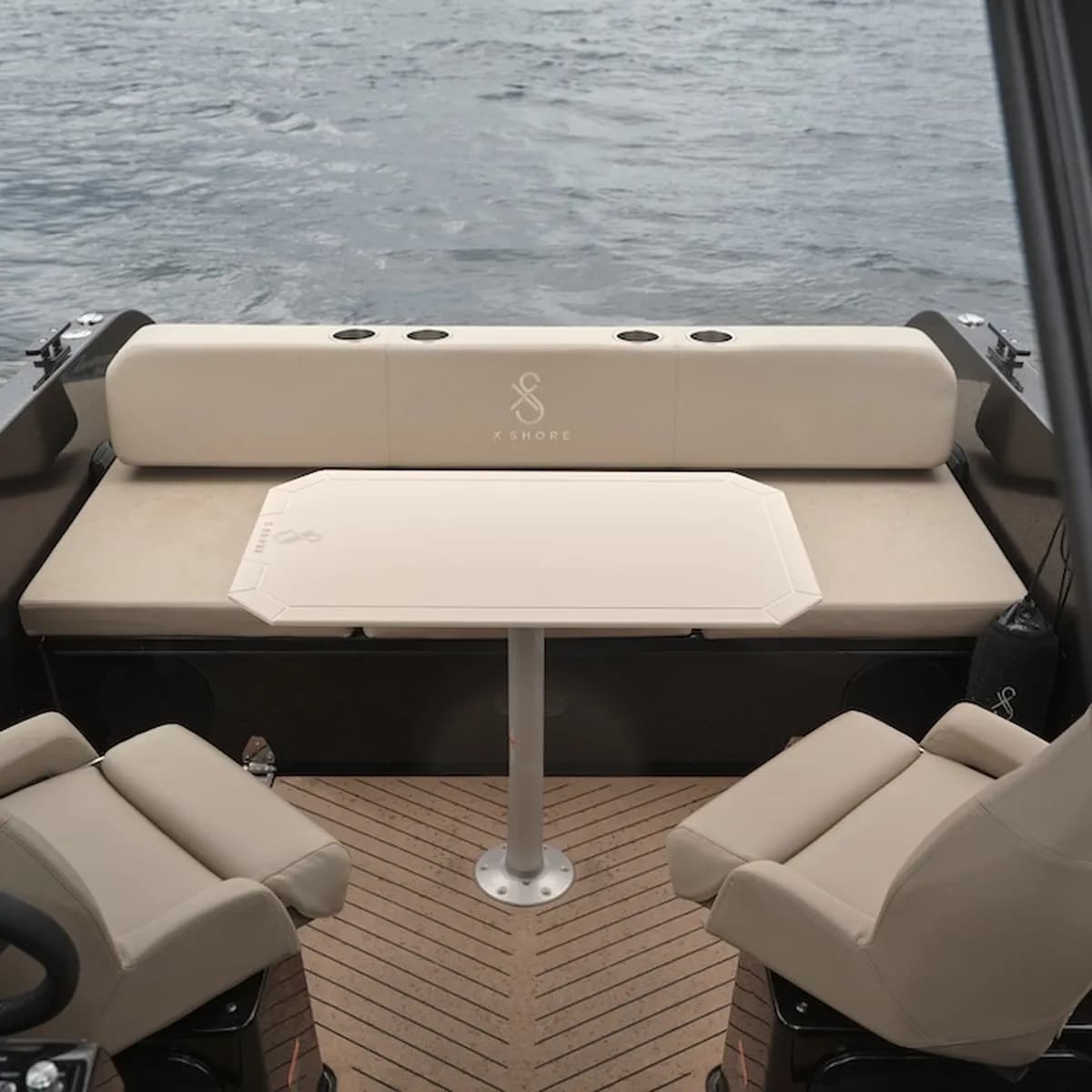 X Shore XS1 cockpit and rear seating area viewed from the helm, with a central table and water visible beyond the stern.