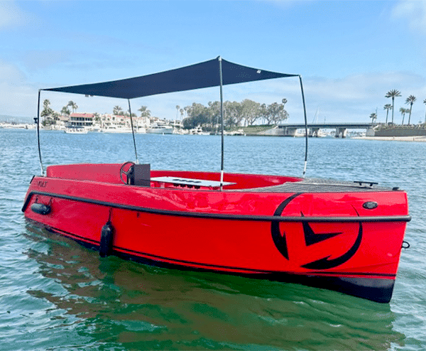 Vision Marine Volt 180 viewed from the side on the water, showing its red hull and raised sunshade.