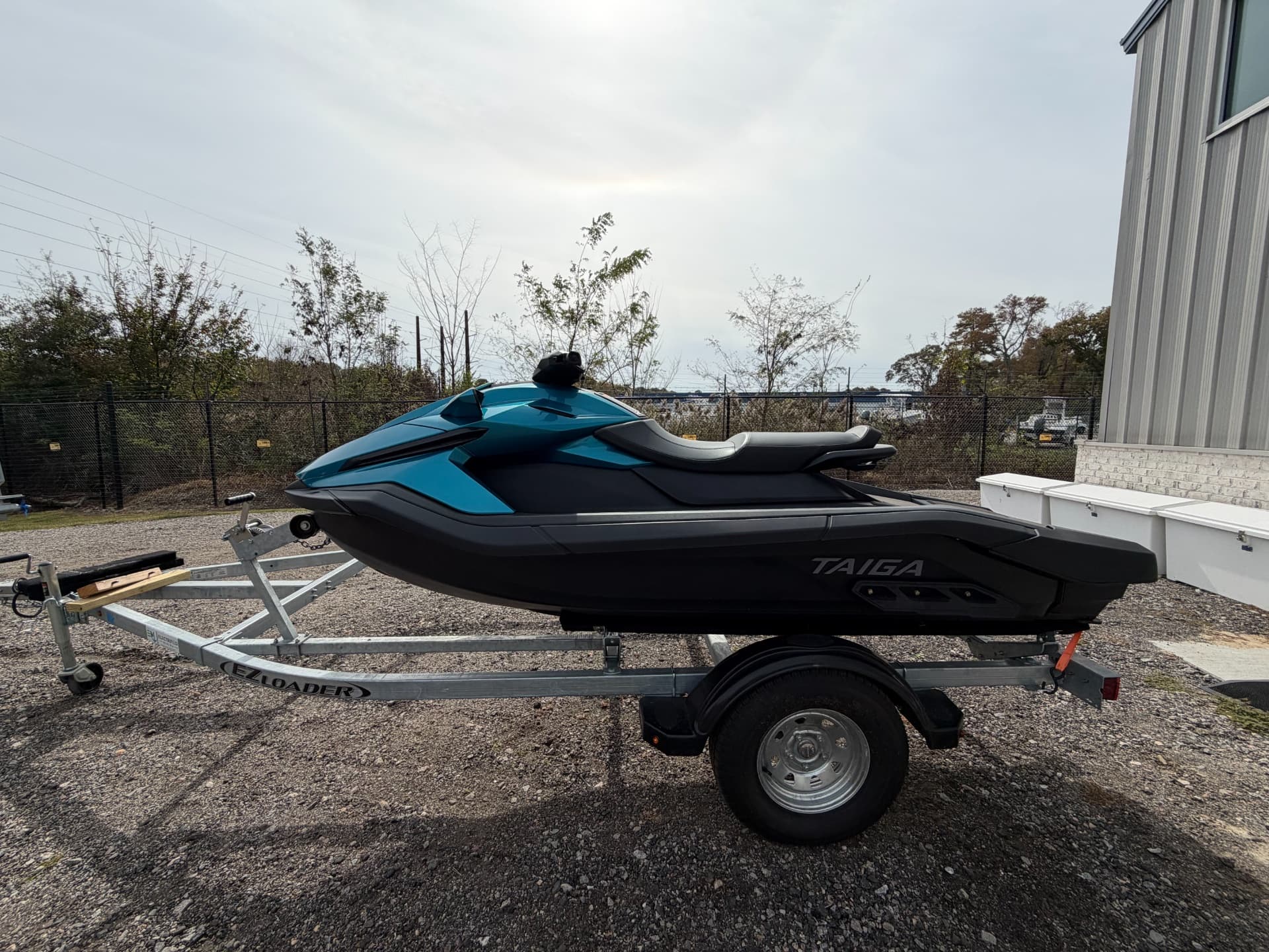Side view of a Taiga Orca WX3 personal watercraft on a trailer beside a building.