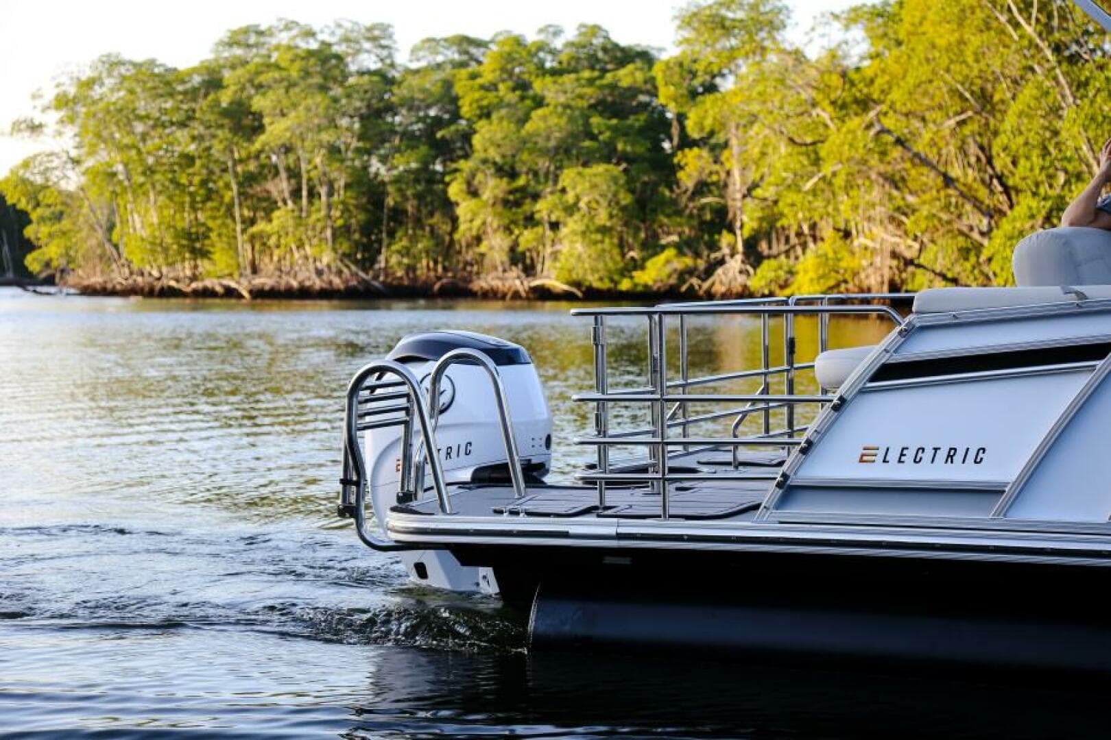 Vision Marine V24 stern and starboard side with visible electric motor, railings, and wake on a wooded waterway