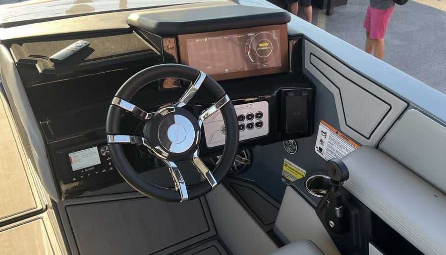 Helm and driver’s console of a boat (2023 Ingenity 23E), viewed from the cockpit, with steering wheel, touchscreen display, controls, and throttle visible.