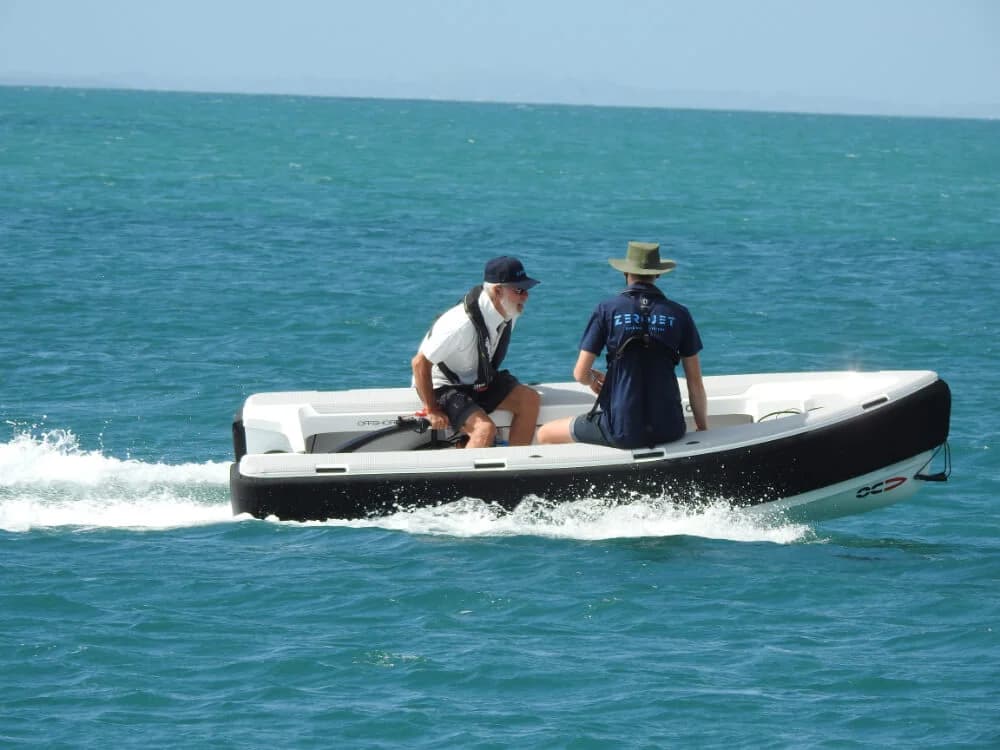 Side view of an OC350 tender underway on open water, with two people seated in the open cockpit.