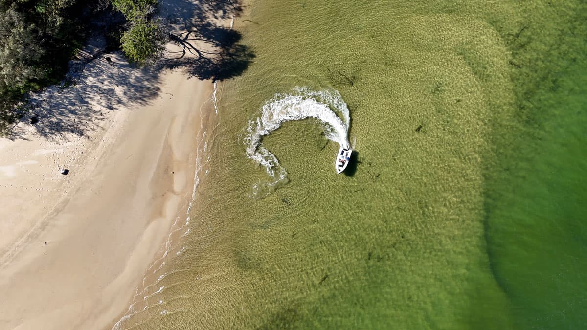 Aerial view of a 2026 Offshore Cruising Tenders OC350 turning in shallow water beside a sandy shoreline.