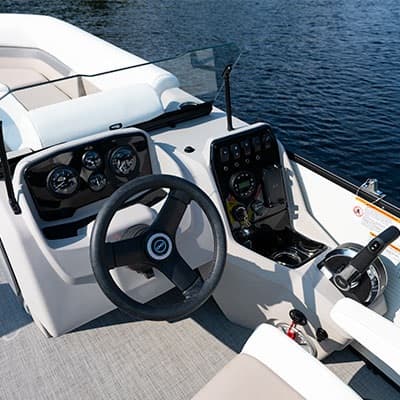 Helm and controls viewed from above in the cockpit of a pontoon boat (2026 Princecraft Vectra 19 L), with steering wheel, gauges, switch panel, and throttle visible.