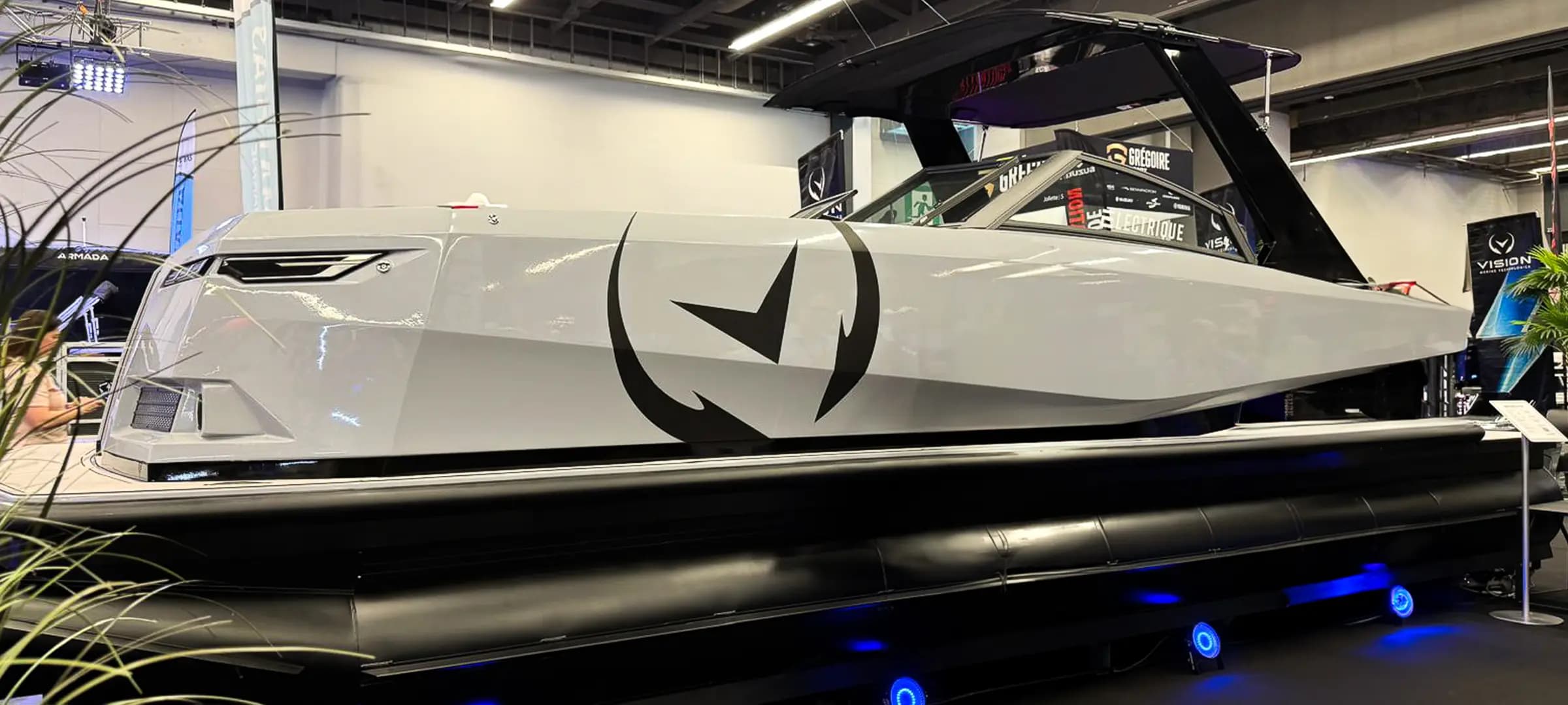 Side view of a white Vision Marine SPECTR boat displayed indoors, showing the hull, pointed bow, black canopy, and twin pontoons.