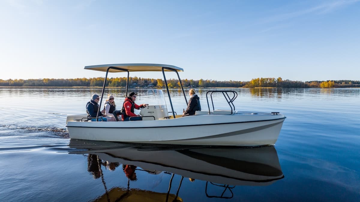 Elvene Amber motorboat viewed broadside on calm water, with several people aboard and a shoreline in the background