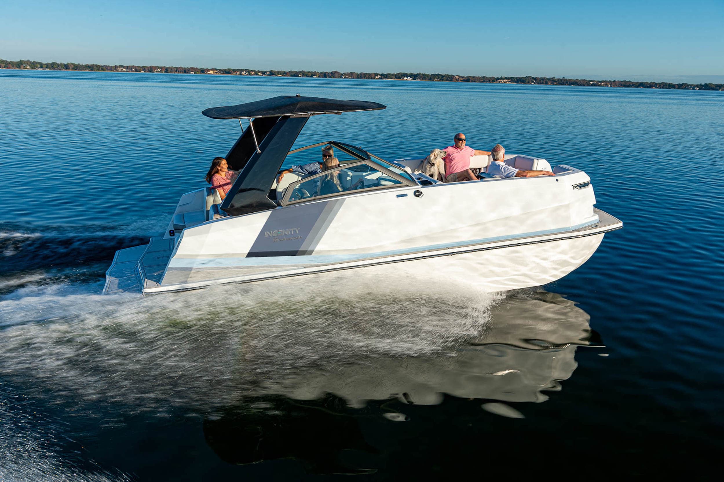 Side view of a 2023 Ingenity 23E motorboat cruising across calm water, with passengers aboard and spray along the hull.
