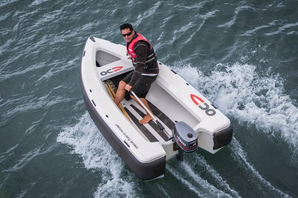 Aerial view of a person steering a 2026 Offshore Cruising Tenders OC350 with an outboard motor, moving through open water.