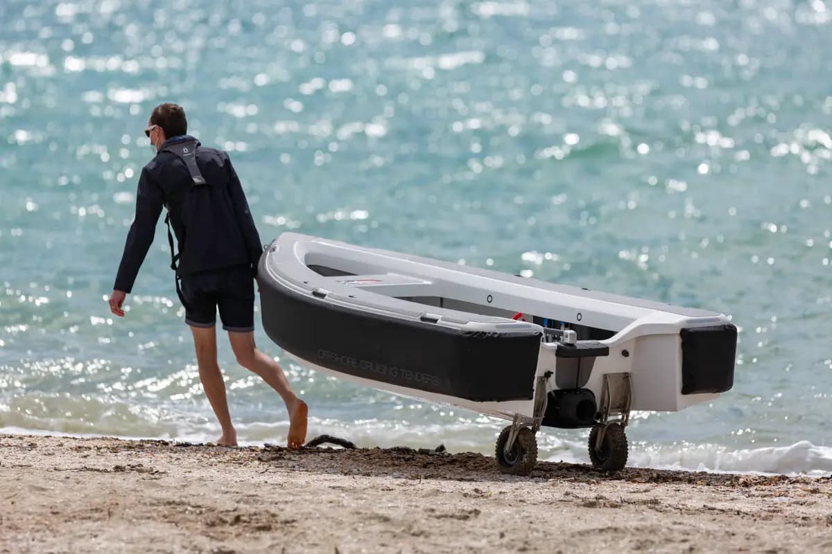 OC330 tender viewed from the side on a beach, with a person pulling it on a wheeled dolly beside the water.