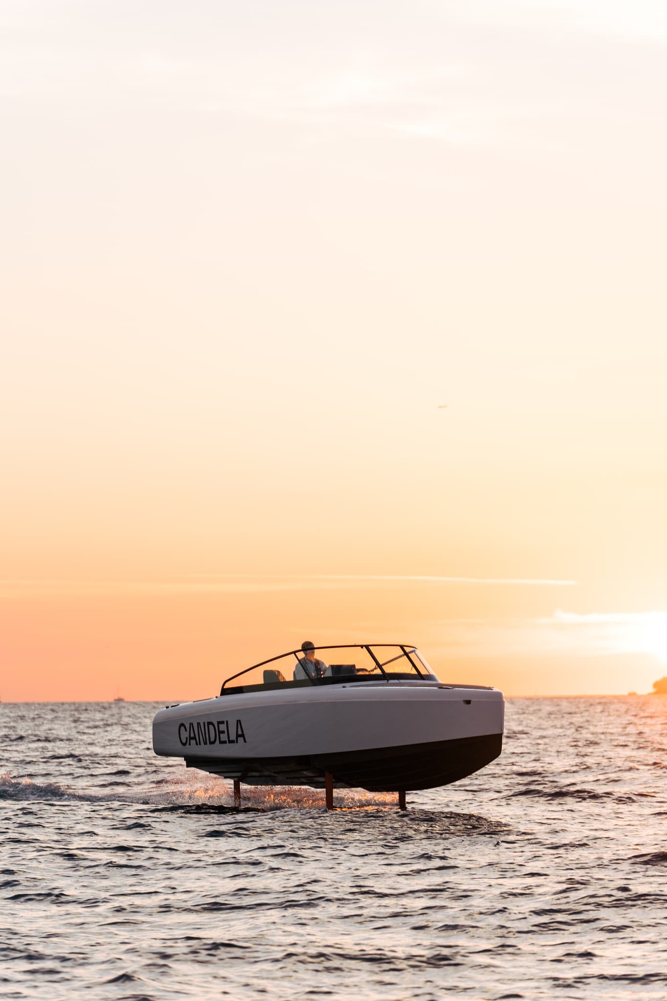 Candela C-8 viewed from the side, hovering above the sea at sunset with its hull and foils visible
