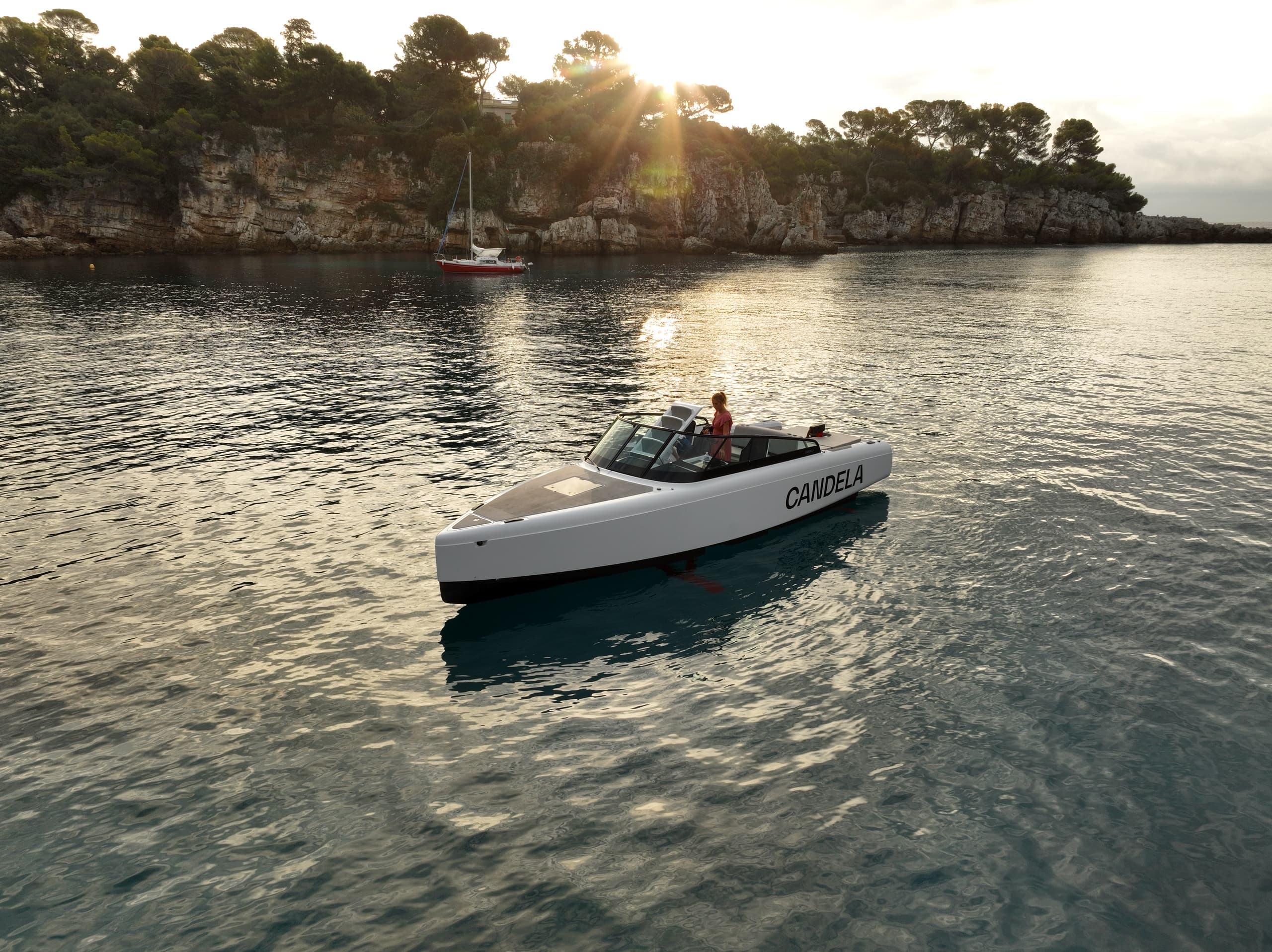 Candela C-8 cruising on calm coastal water, viewed from above with sunlit cliffs in the background