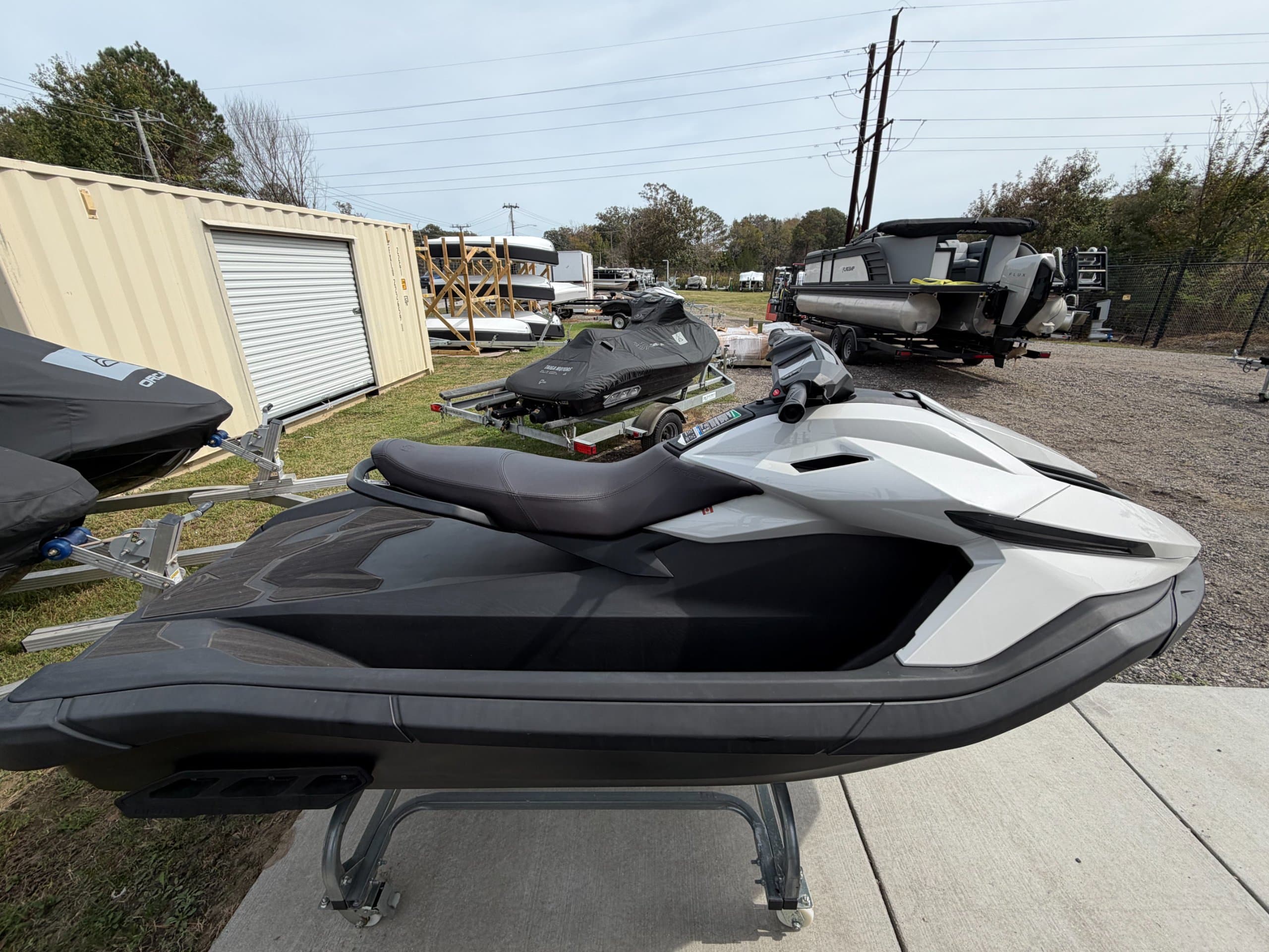 Side view of a white and black personal watercraft on a display stand, with other watercraft and trailers in the background.