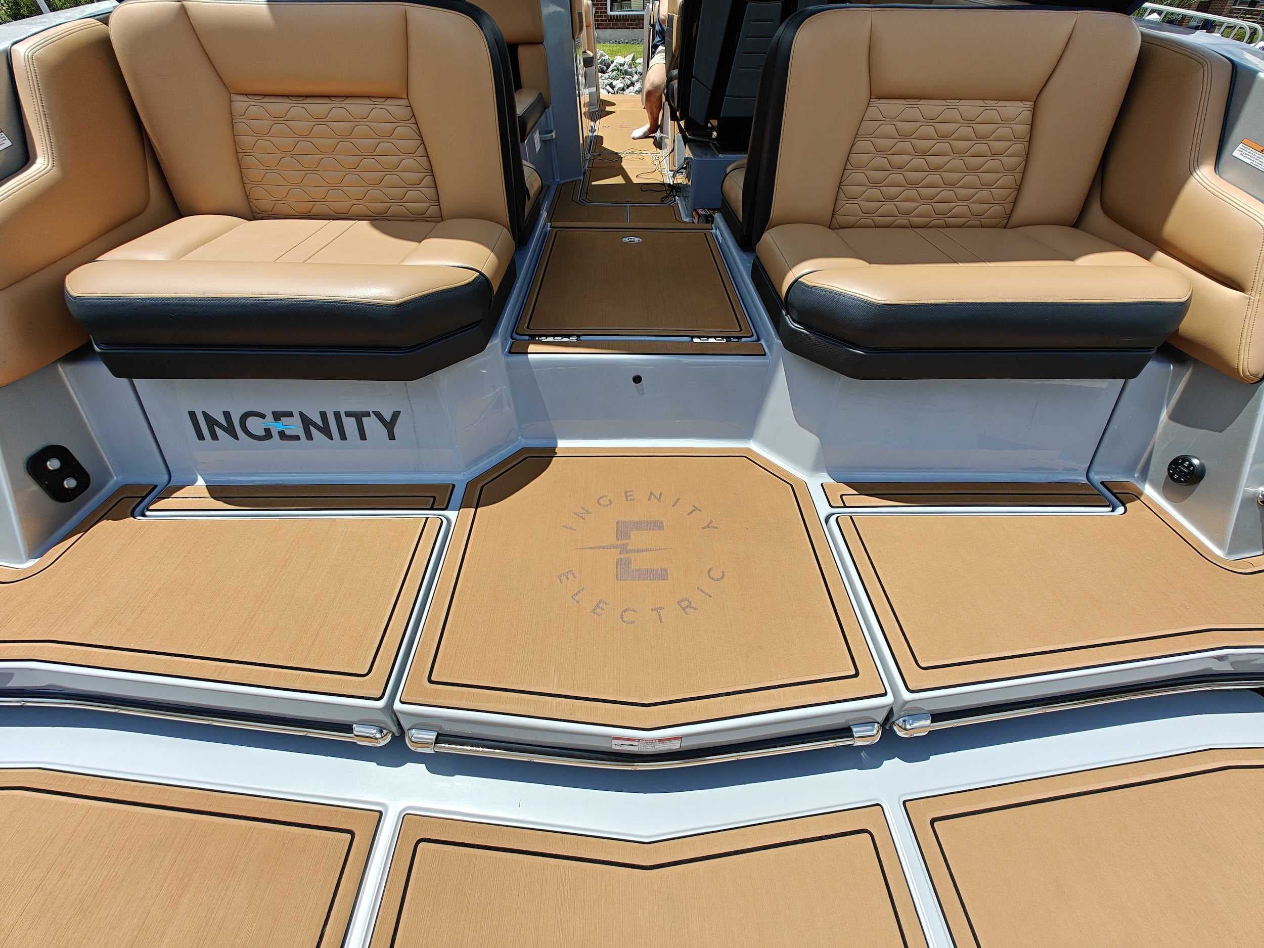 View from the swim platform into the cockpit of an Ingenity 23E, showing tan seating, deck mats, and Ingenity branding.