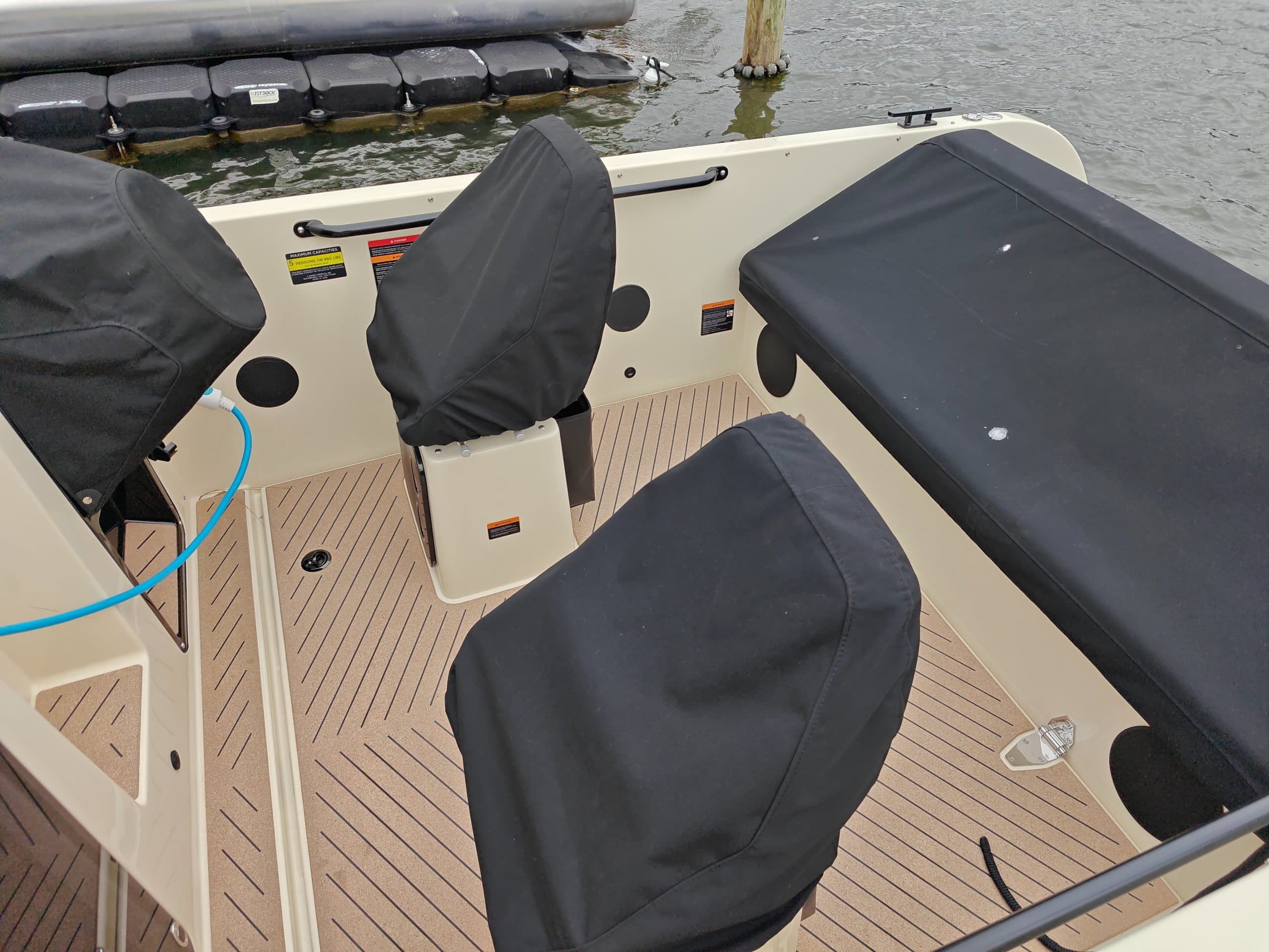 2024 Vision Marine Fantail 217
Open cockpit of a cream-colored electric boat with covered seats, teak-style flooring, and docked watercraft in the background