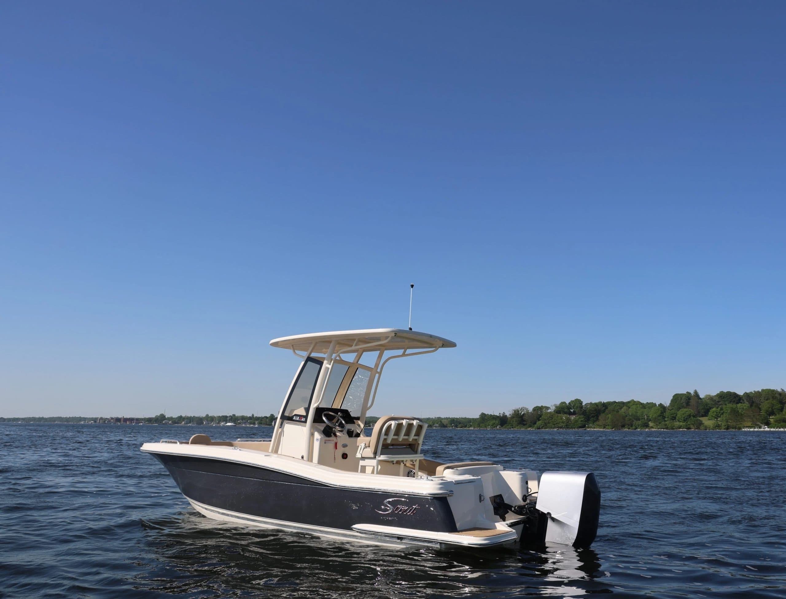 Scout 215 XSF center-console boat with tan T-top and twin outboard motors cruising on a lake under a clear blue sky