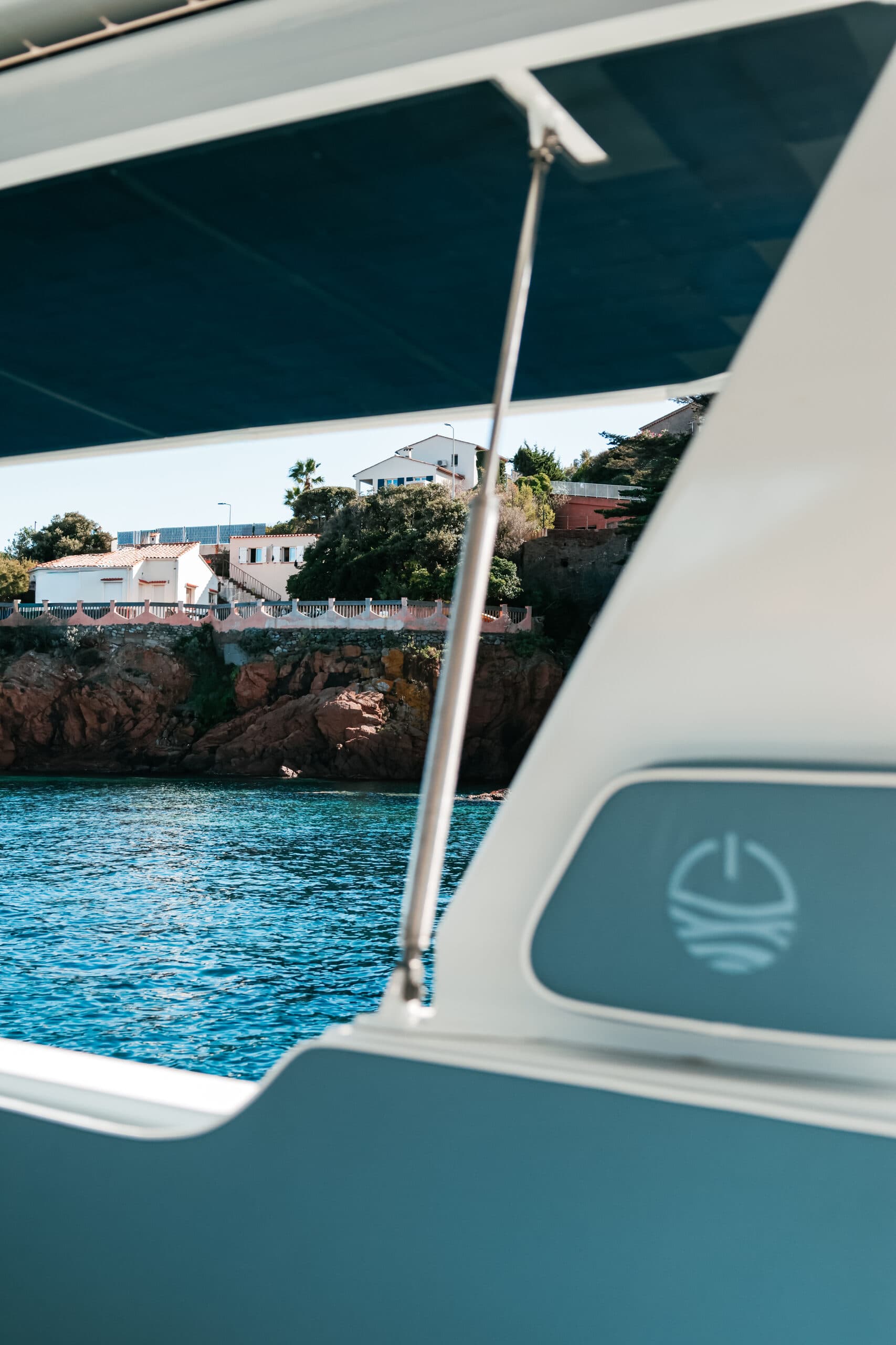 View from the Millikan M10 boat toward turquoise water and a rocky shoreline, framed by the canopy and side panel.