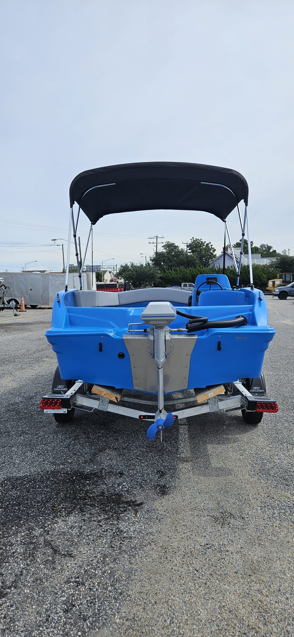 Rear view of a blue Vision Marine Phantom electric boat on a trailer, with a black canopy and marina visible in the background.
