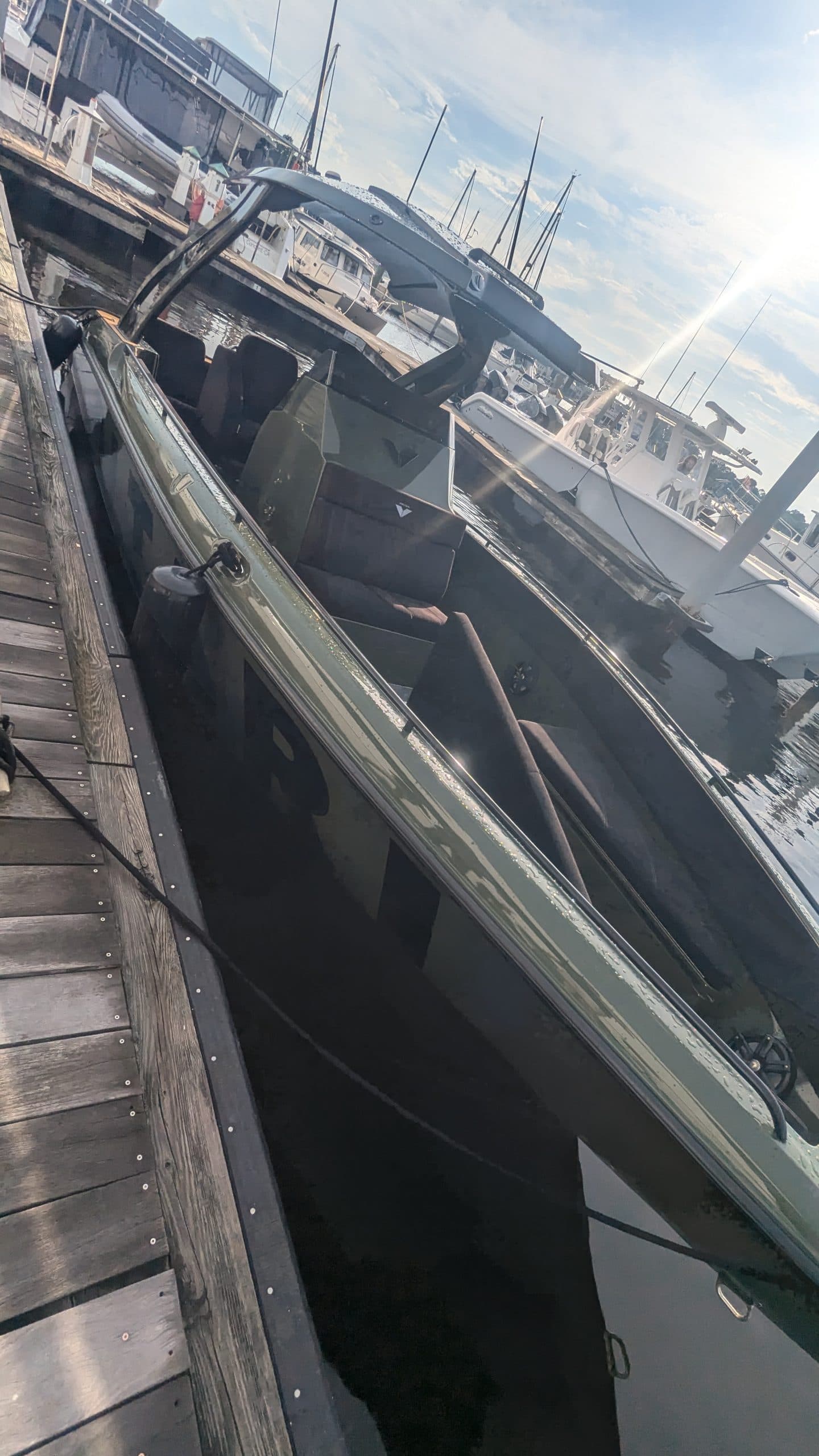 Voltari 260E electric boat moored beside a marina dock, viewed from above with other boats and harbor structures in the background.