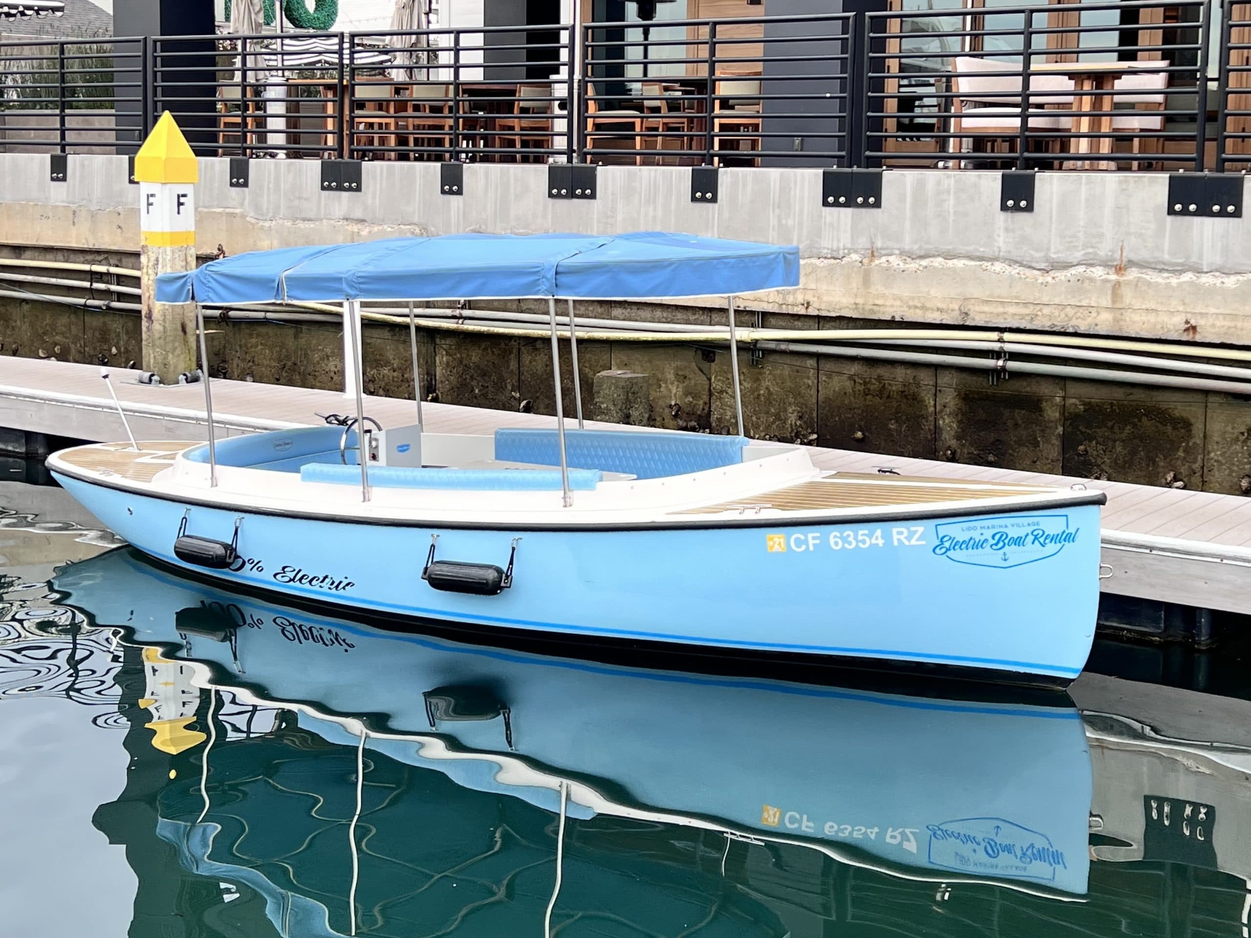 2024 Vision Marine Fantail electric boat docked in calm water, with a light-blue hull, blue canopy, and side seating.