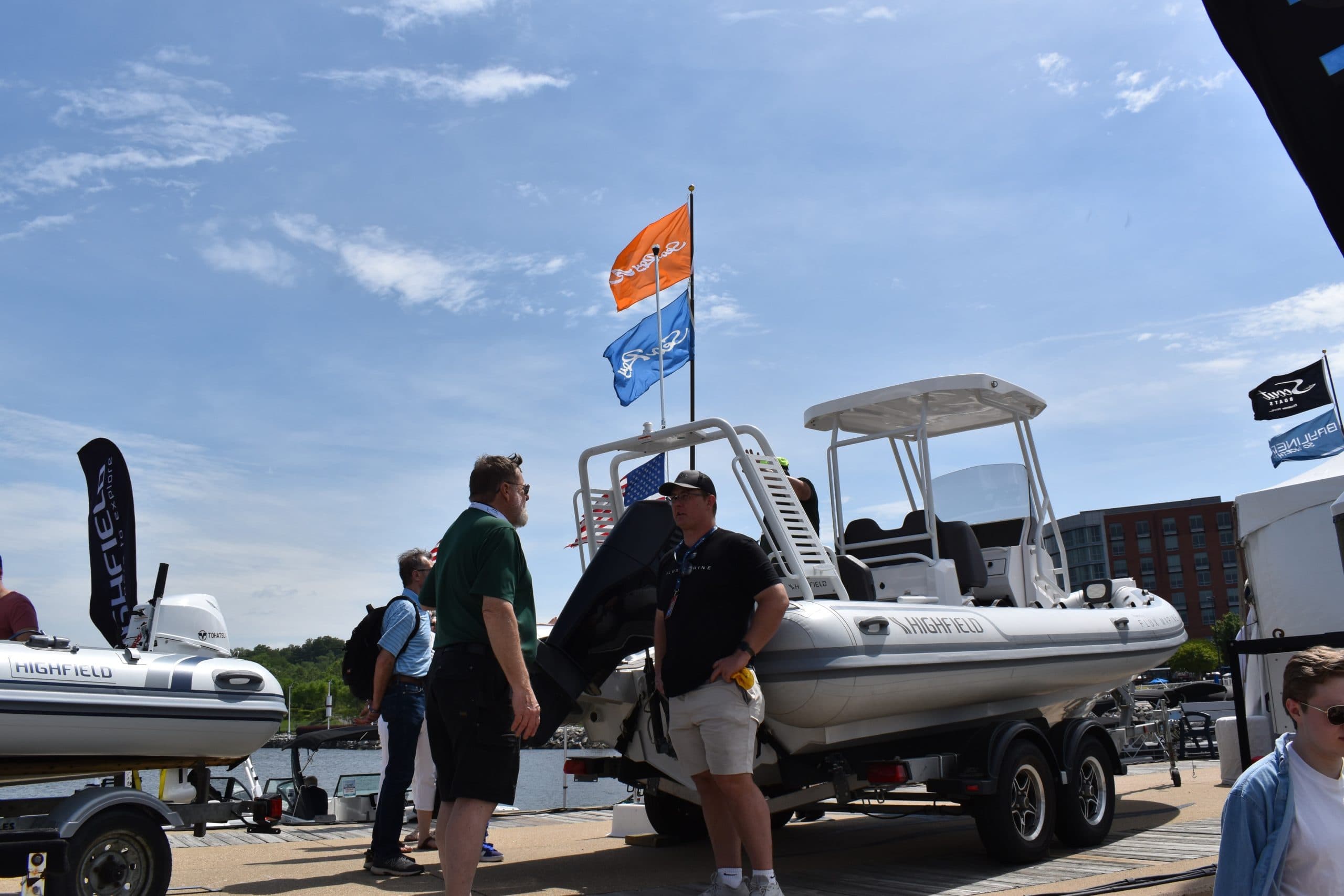Highfield Sport 660 rigid inflatable boat on a trailer at a marine show, with a console, T-top, outboard motor, and flags.