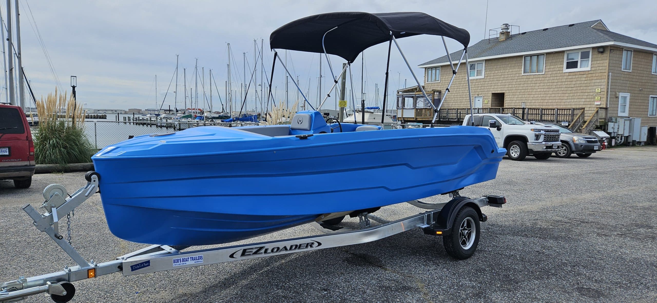 Blue Vision Marine Phantom boat on a trailer with a black canopy, parked near a marina.