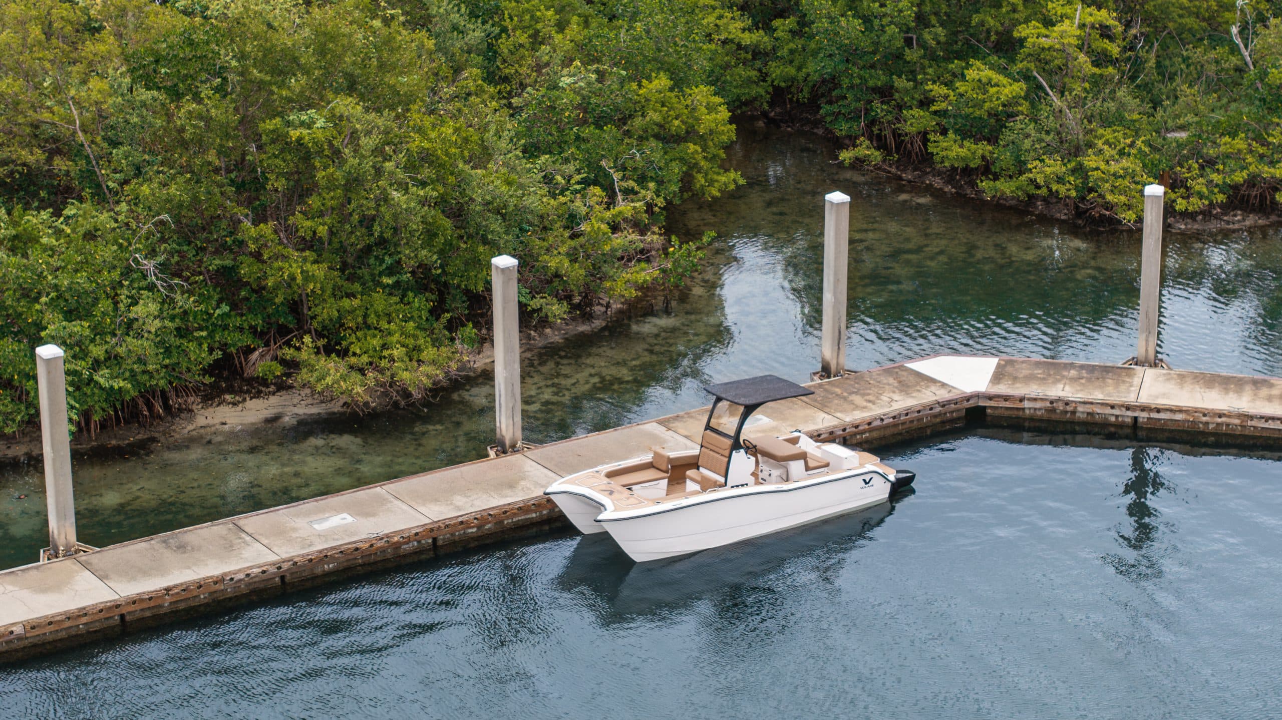 White catamaran Artemis 23 boat docked beside a dock in a narrow, tree-lined waterway.