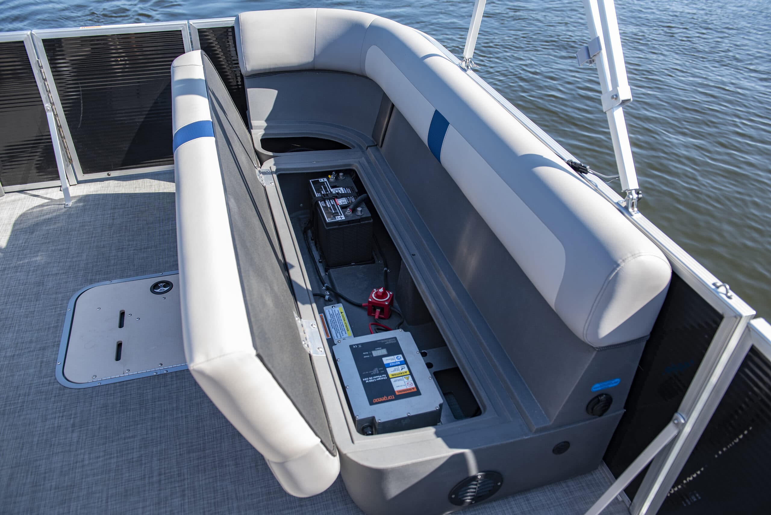 Interior of a Princecraft Brio E17 electric pontoon boat with cushioned seating lifted showing battery compartment, water in background