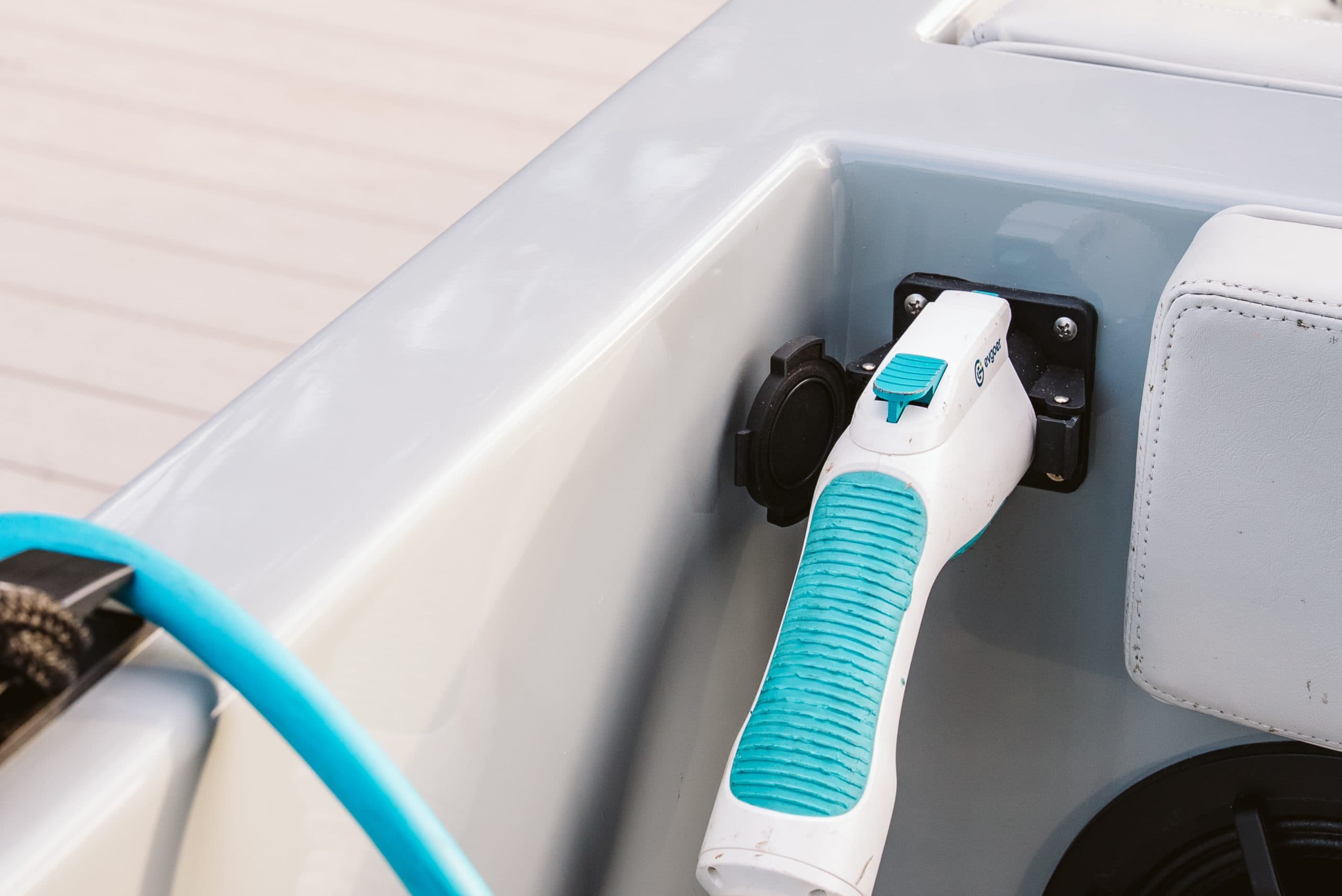 Electric boat charger connected to a charging port beside a seat, with a turquoise electric vehicle cable connector plugged in.