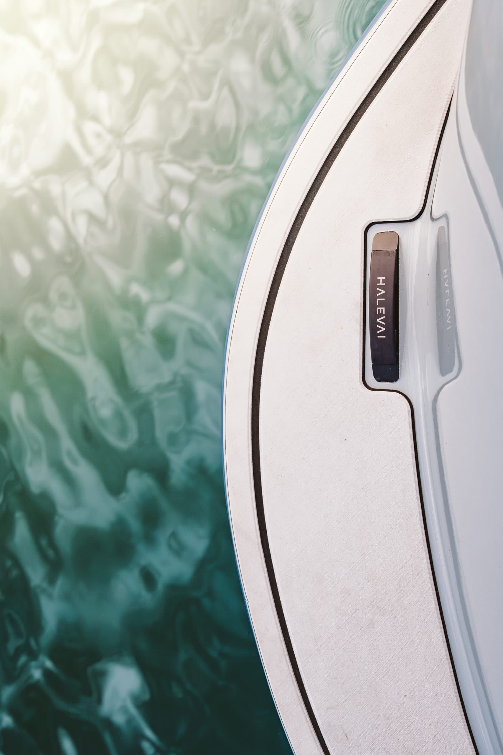 Close-up of a Halevai model2050’s white deck with dark trim, viewed beside rippling green water.