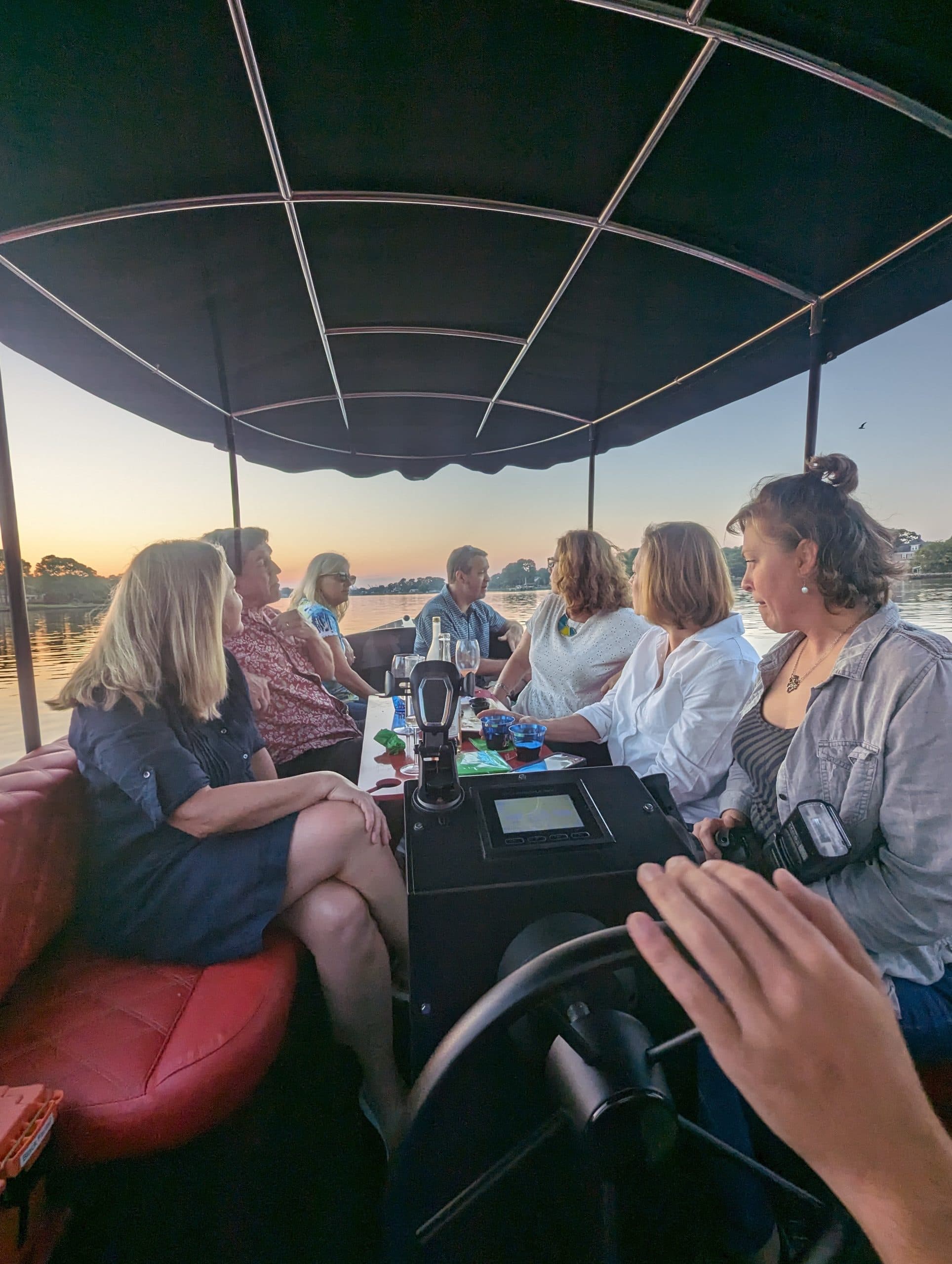 Passengers seated under a canopy aboard a Fantail boat, with a central helm console and sunset-lit water in the background.