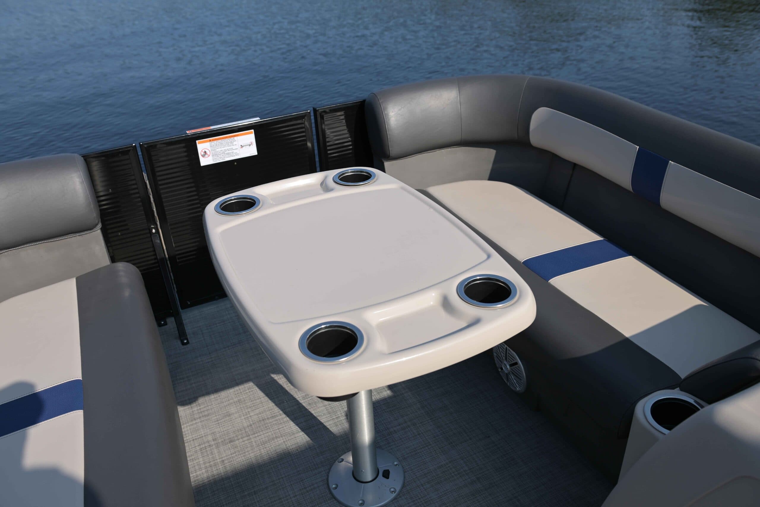 Interior seating and table of a Princecraft Brio E17 with cup holders, cushioned benches with blue accent line, and carpeted deck. There is a popup table in front of the bench