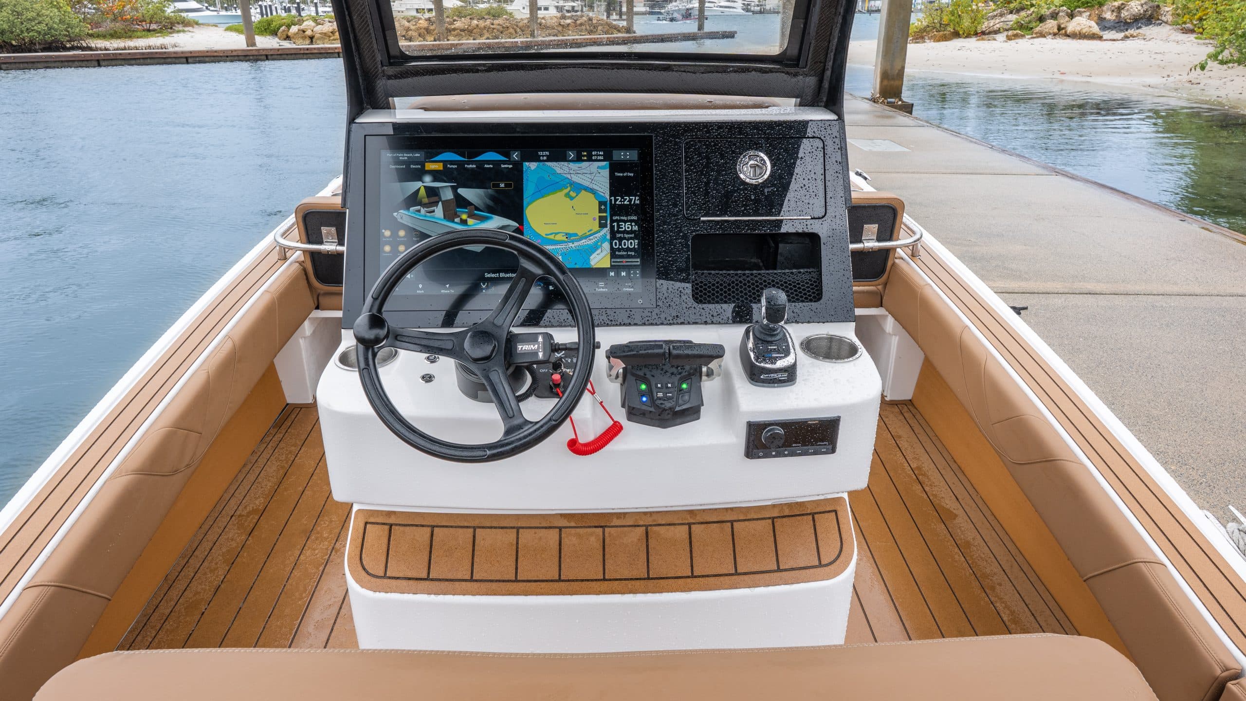 White helm and dashboard of Artemis23, featuring a steering wheel, digital displays, controls, and cushioned seating by the water.