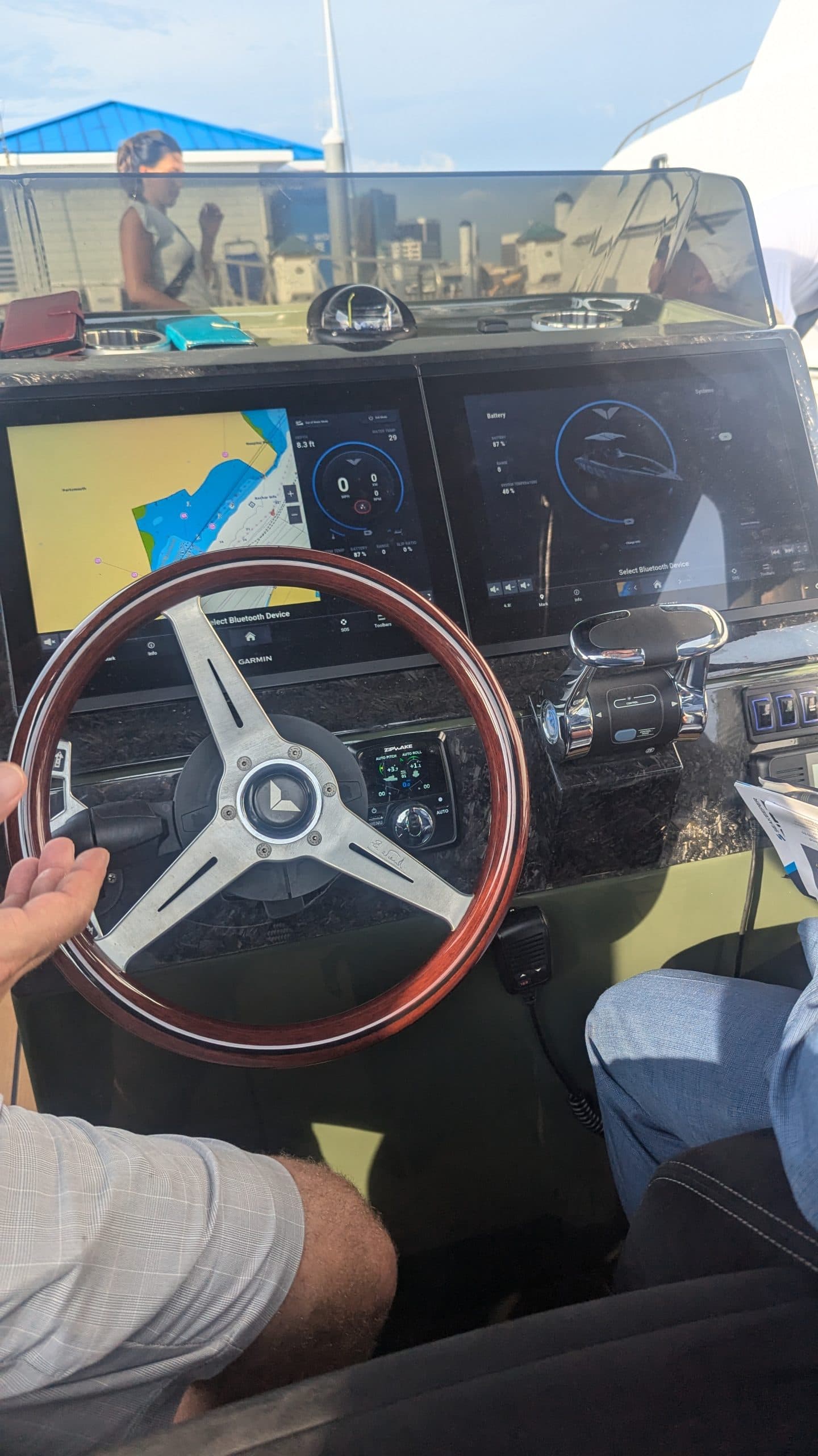 Voltari 260E helm with wood-rim steering wheel, dual digital displays, navigation map, windshield, and seated passengers.