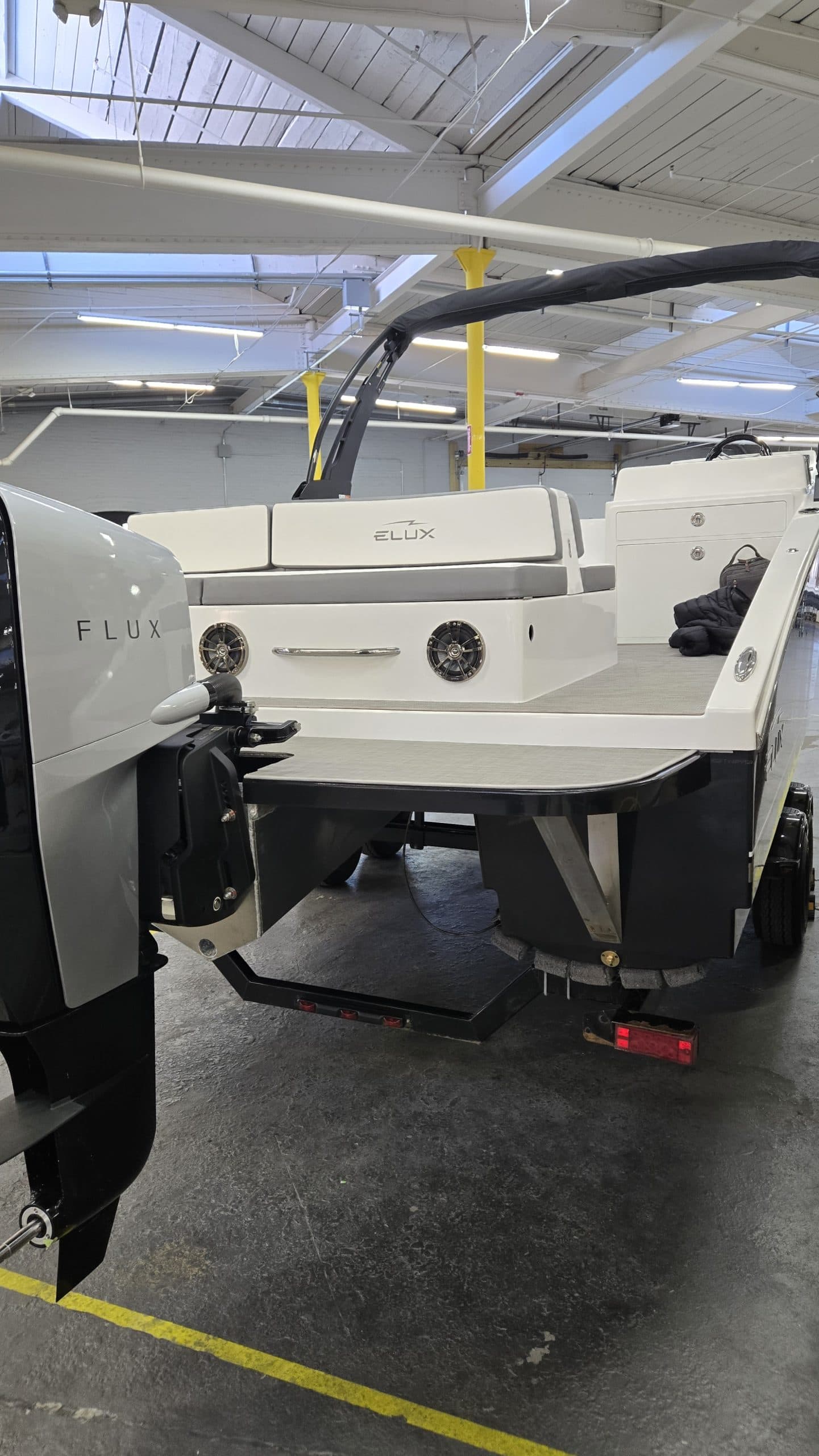 Rear view of a white Flux Marine GFX Stealth electric boat displayed indoors, showing outboard motor, swim platform, and seating.