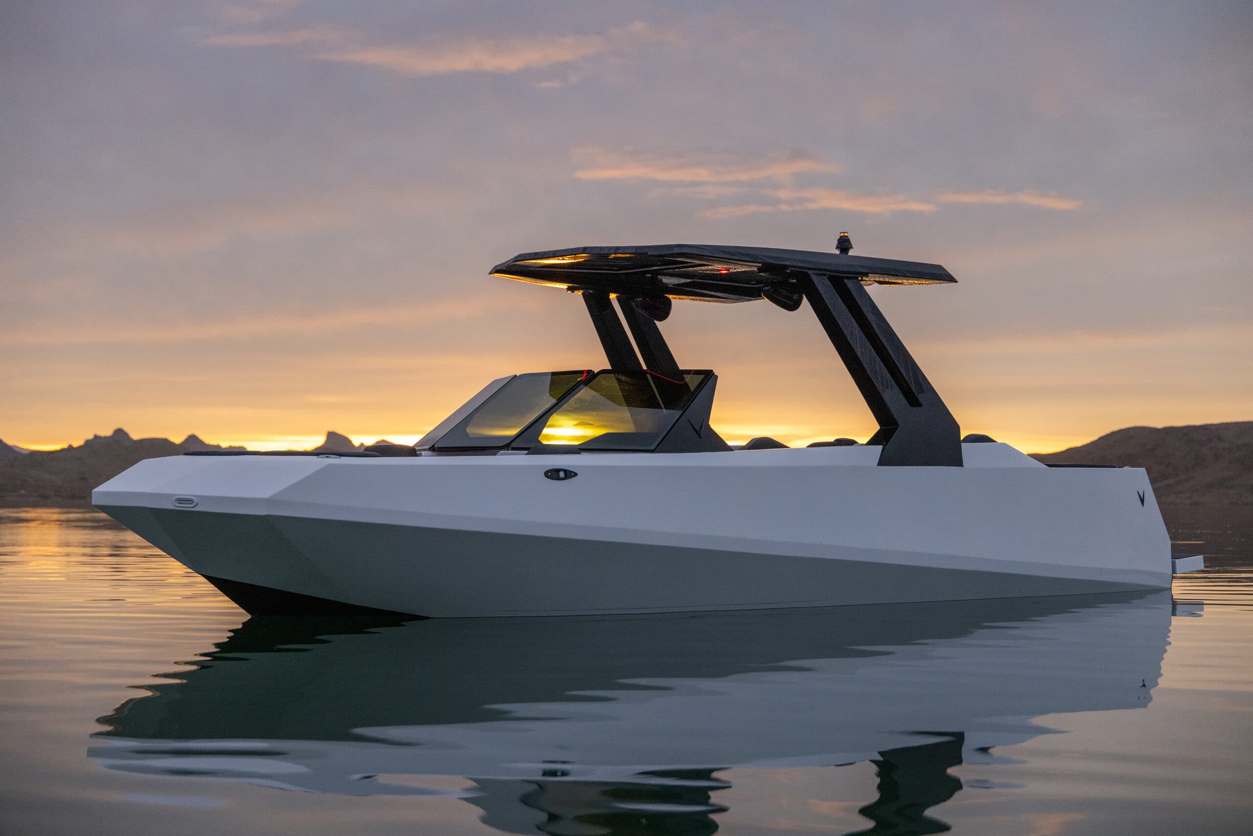 Voltaic AEW24 electric boat floating on calm water at sunset, showing its angular hull, canopy, and windshield.