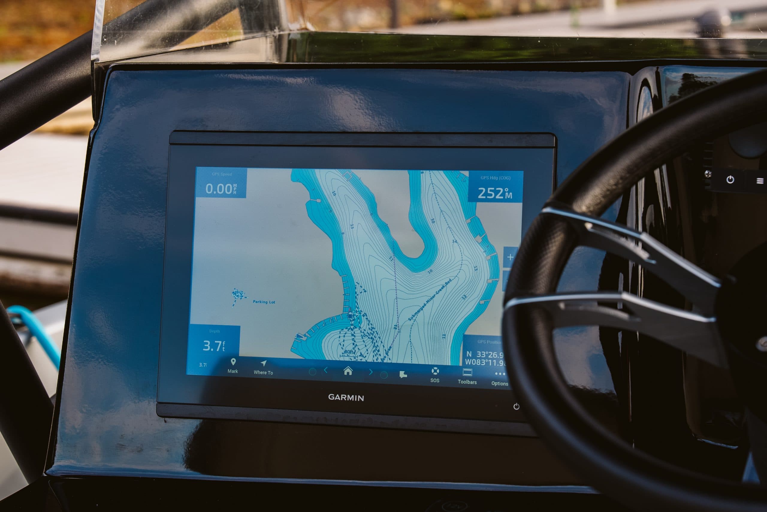 Garmin marine navigation display showing a nautical chart, mounted on the dashboard beside the steering wheel.