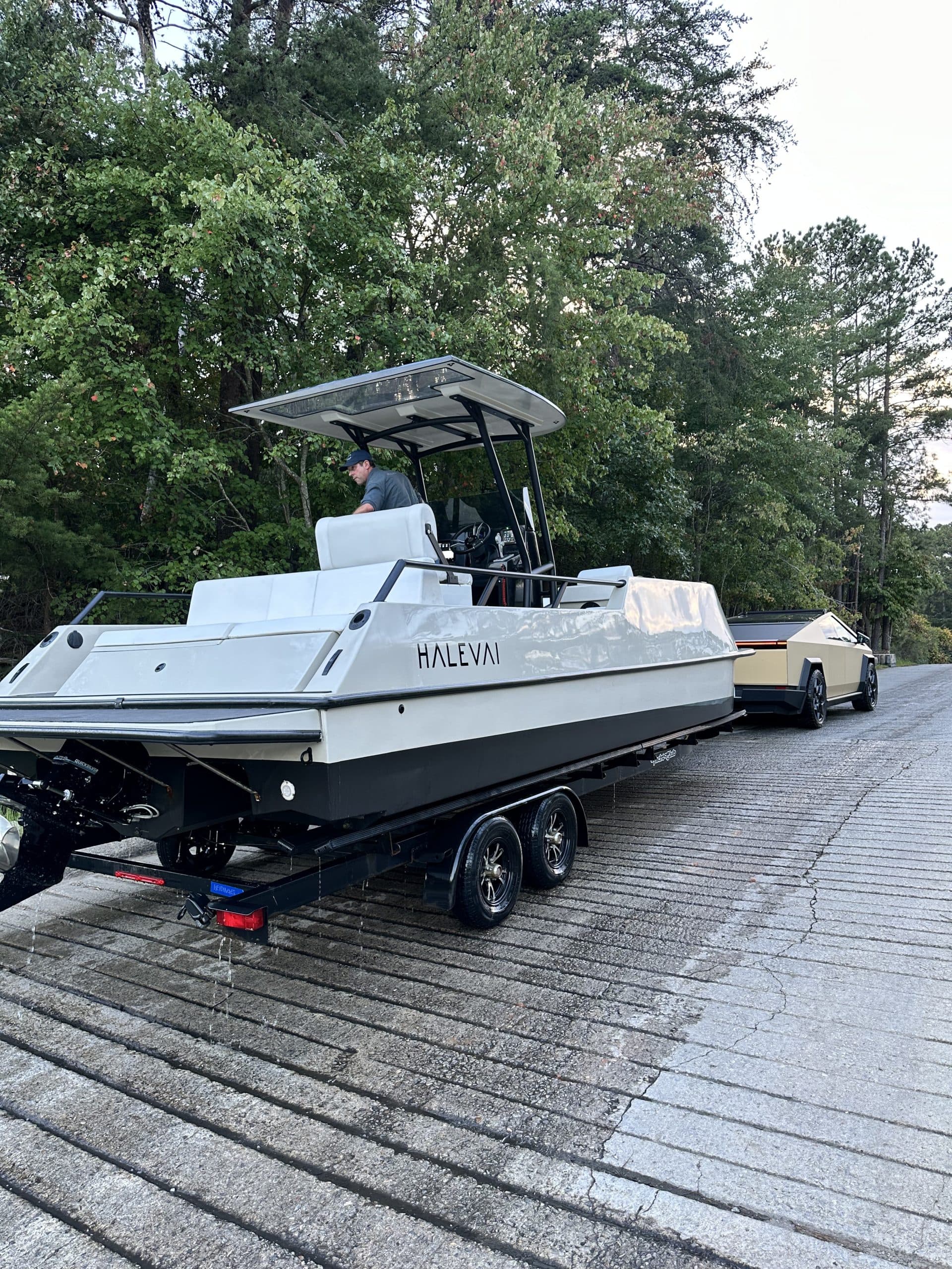 Halevai Model 2050 electric boat on a trailer, featuring a canopy, center console, and white hull in a tree-lined parking area.