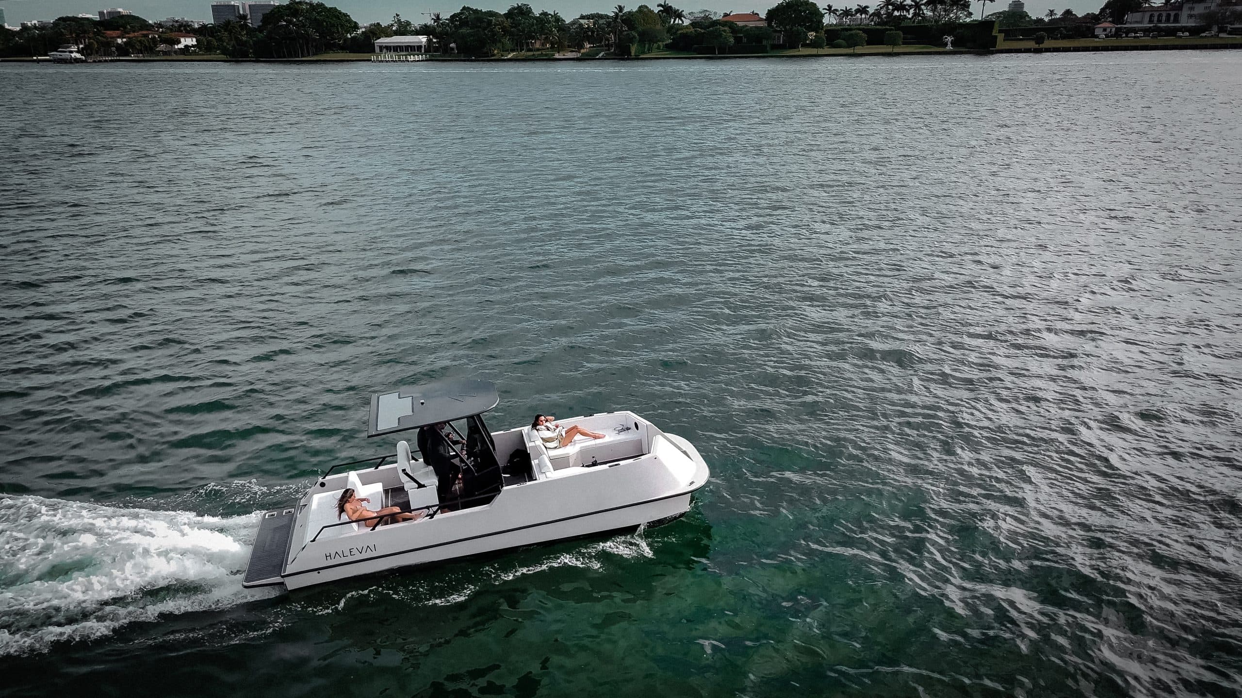 Halevai model2050 boat cruising across a bay, viewed from above and to the side with shoreline in the background