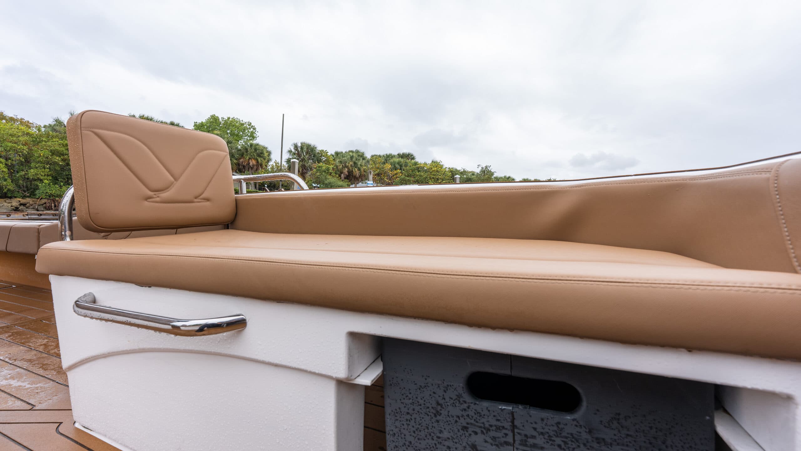 Tan cushioned seating with Volare logo stitching on the headrest ontop of storage area and a white panel with a handle