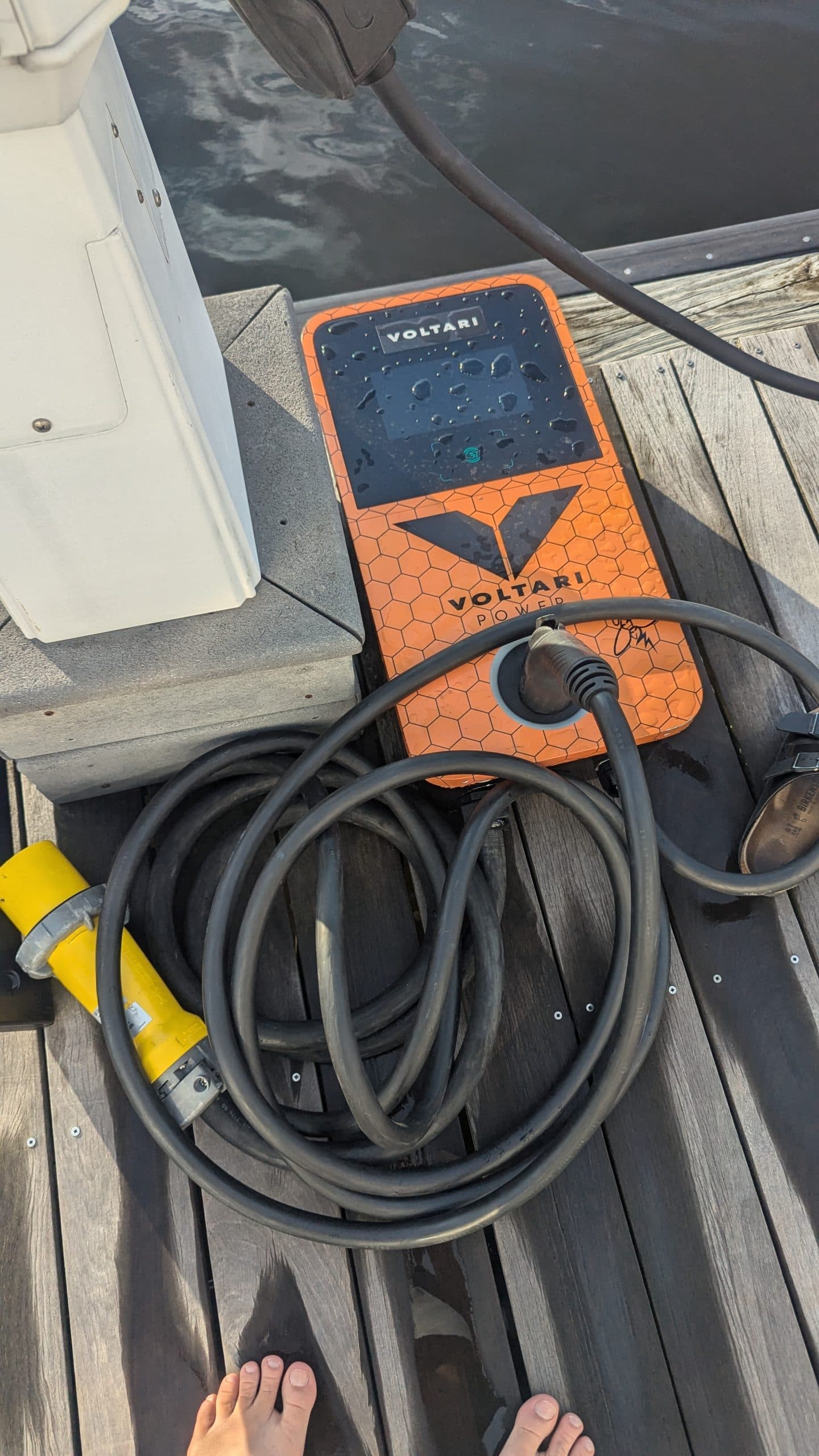 Voltari 260E electric boat charger with coiled cable resting on a dock beside a boat.