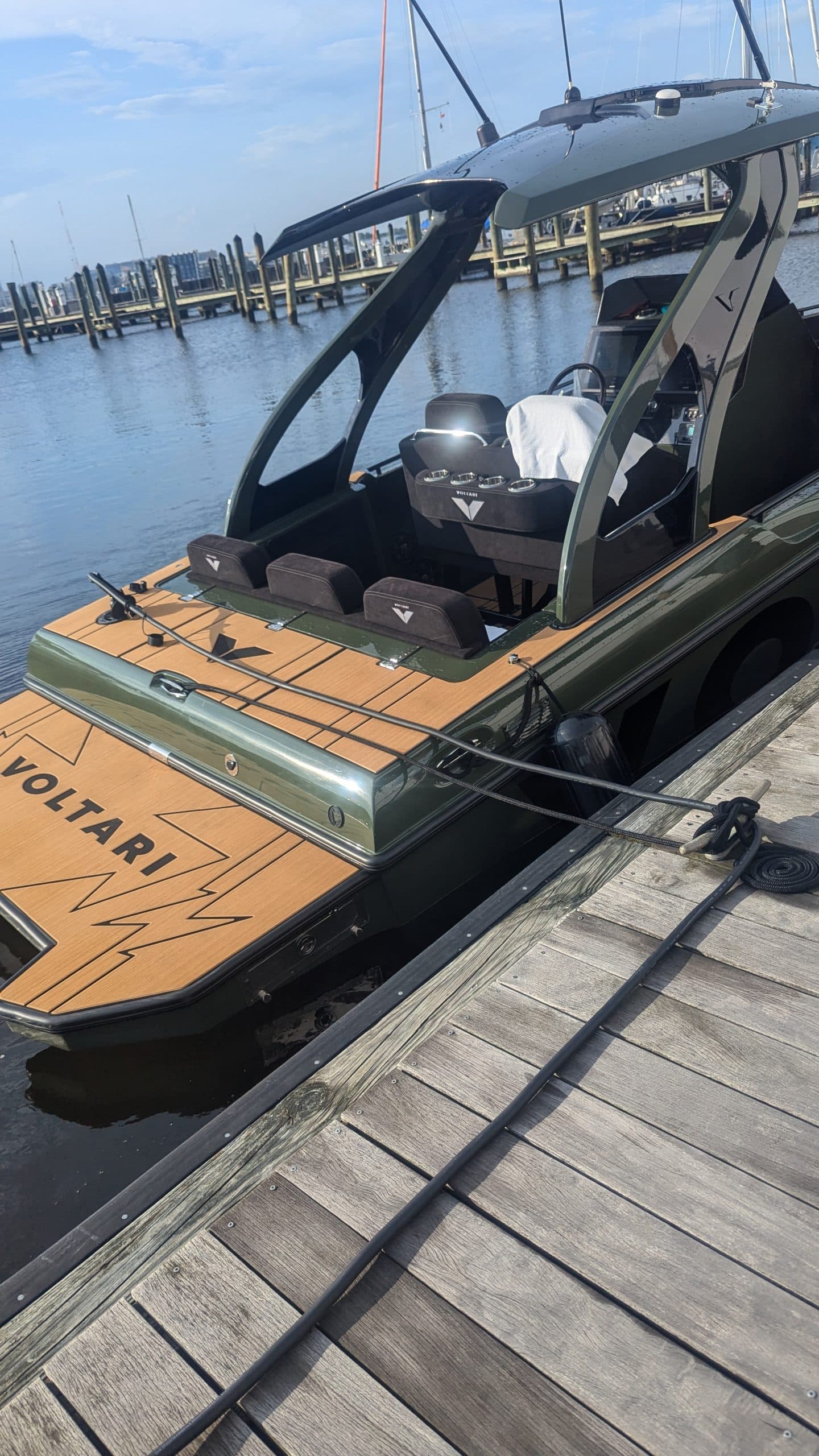 Voltari 260E electric boat docked at a marina, showing its open bow deck, seating, canopy, and dark hull.