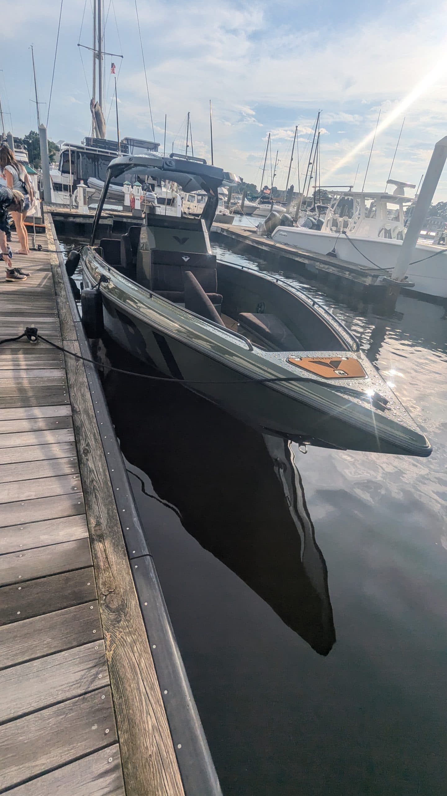 Voltari 260E electric boat moored beside a marina dock, viewed from above with other boats and masts in the background.