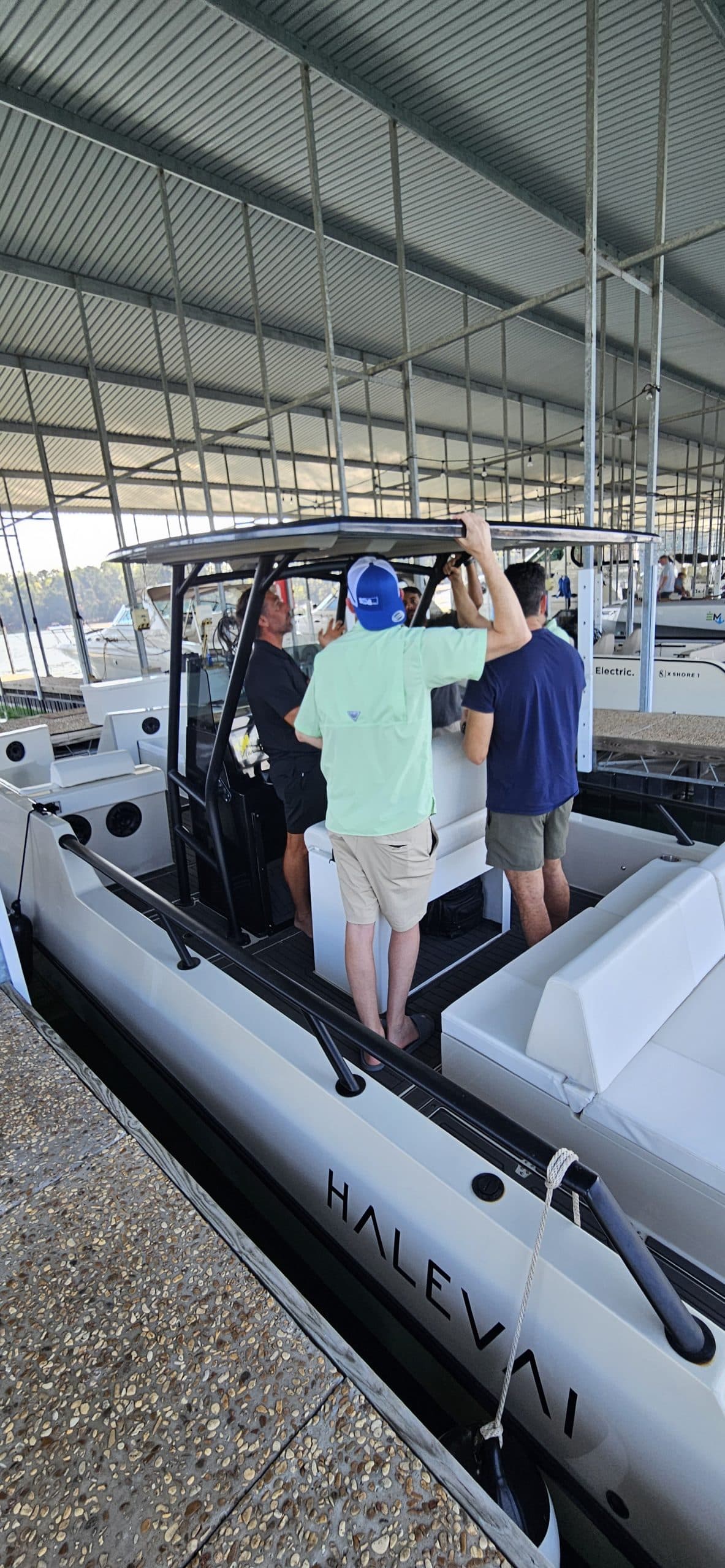 Halevai electric boat displayed in a covered marina, with three people aboard and a visible center console, seating, and canopy.