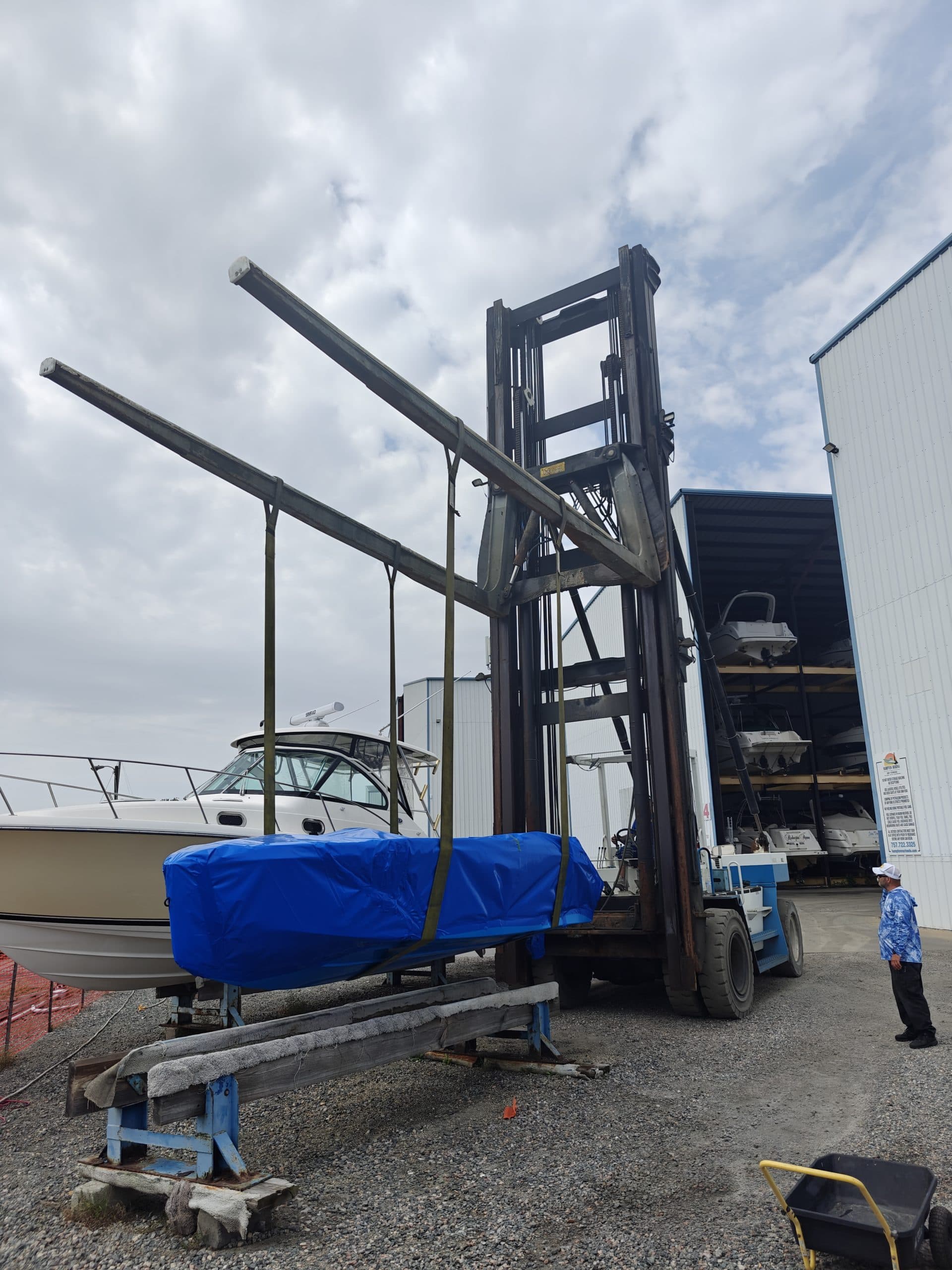 Vision Marine Phantom boat covered in blue tarp beside a forklift at a marina facility.