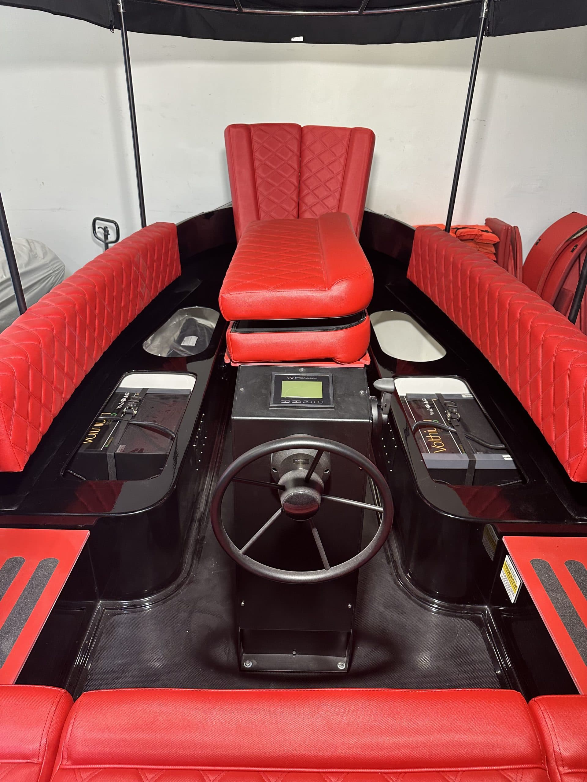 Vision Marina Fantail with red upholstered helm and seating inside a black electric boat, with steering wheel, central display, and side storage compartments.