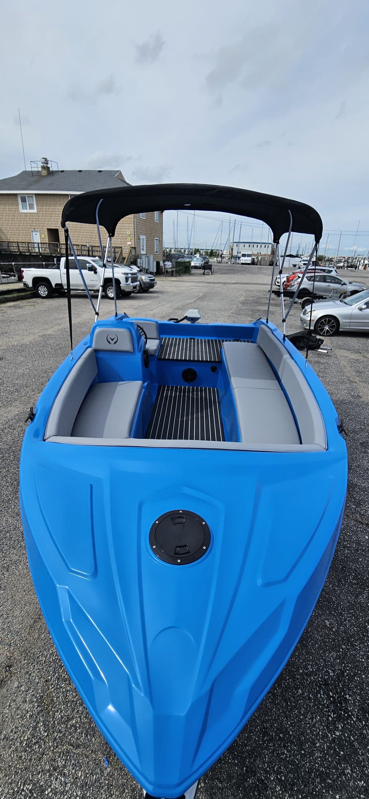 Bright blue electric boat viewed from above, showing its open cockpit, seating, steering console, black canopy, and marina setting.
