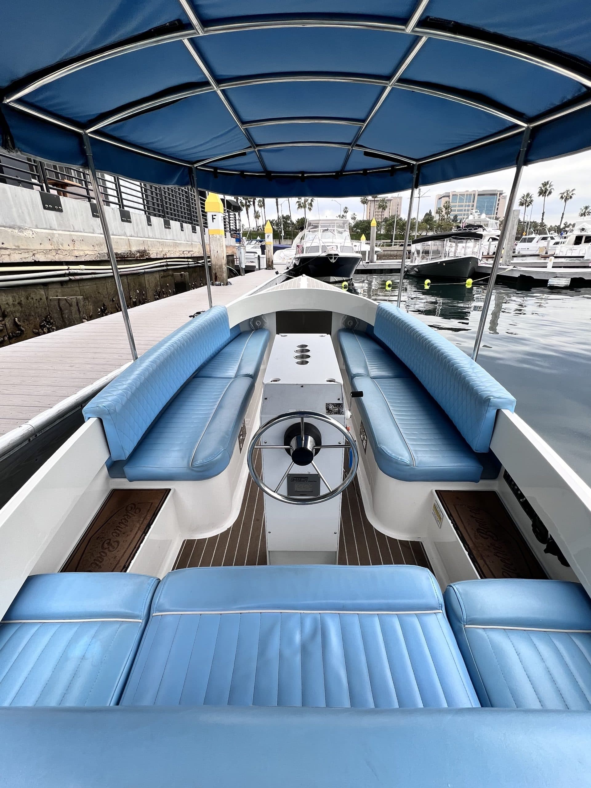 2024 Vision Marine Fantail 217
Interior view of a 2024 Vision Marine Fantail cockpit showing blue upholstered seating, helm, wood-look flooring, and canopy docked at a marina.
